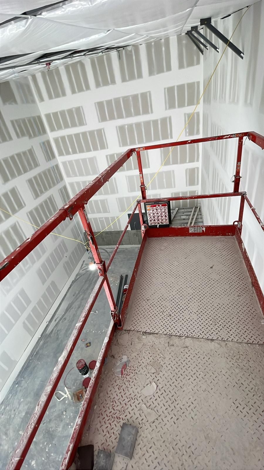Red-railed metal scaffolding platform inside a building under construction with plastic-covered walls and ceiling.