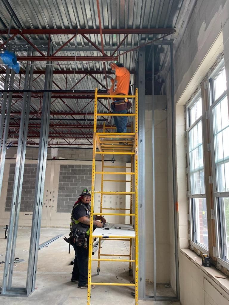 Workers on yellow scaffold in unfinished room with exposed ceiling and windows