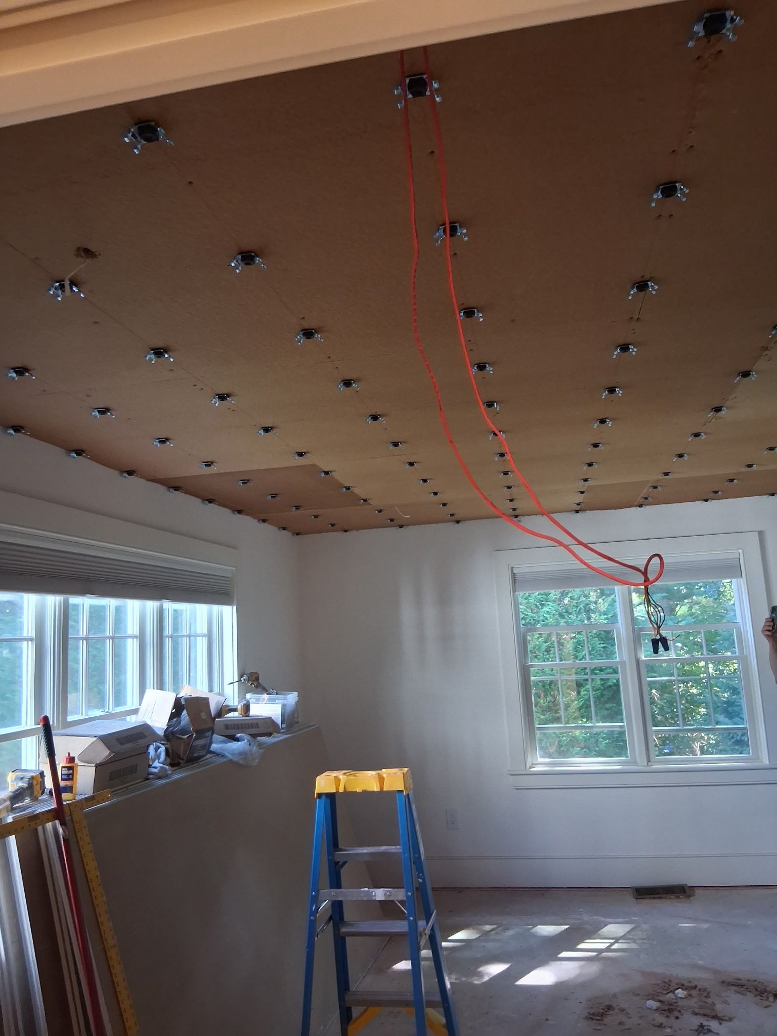 Room under renovation with a ladder and exposed ceiling wiring, sunlight through the windows.