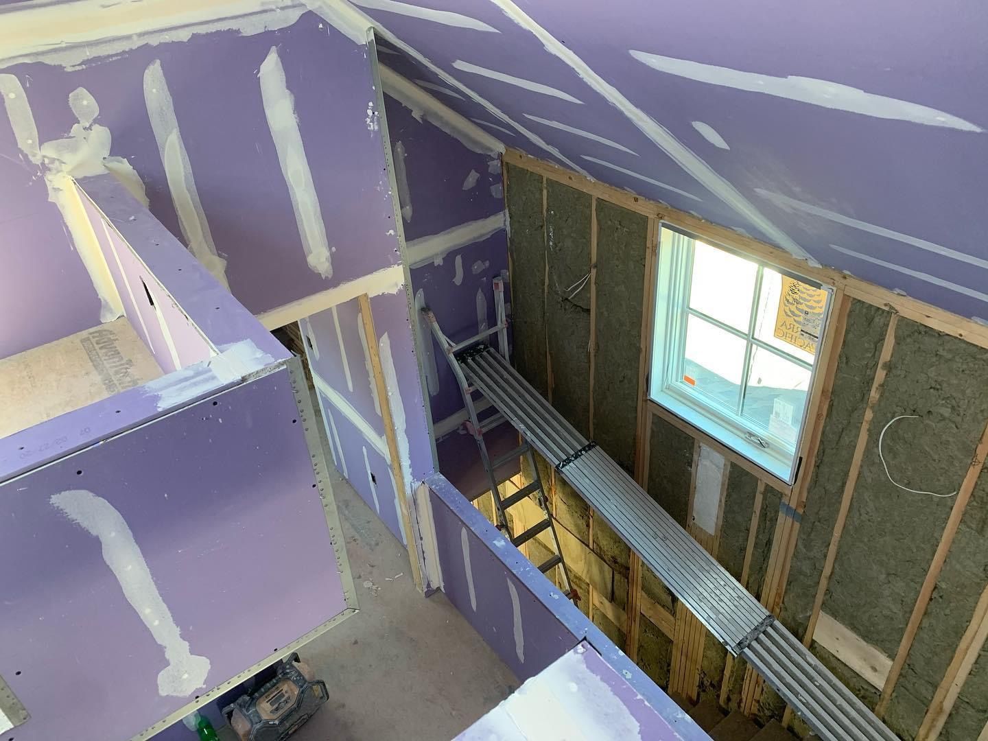 Partially finished interior staircase with purple drywall and a window on the right