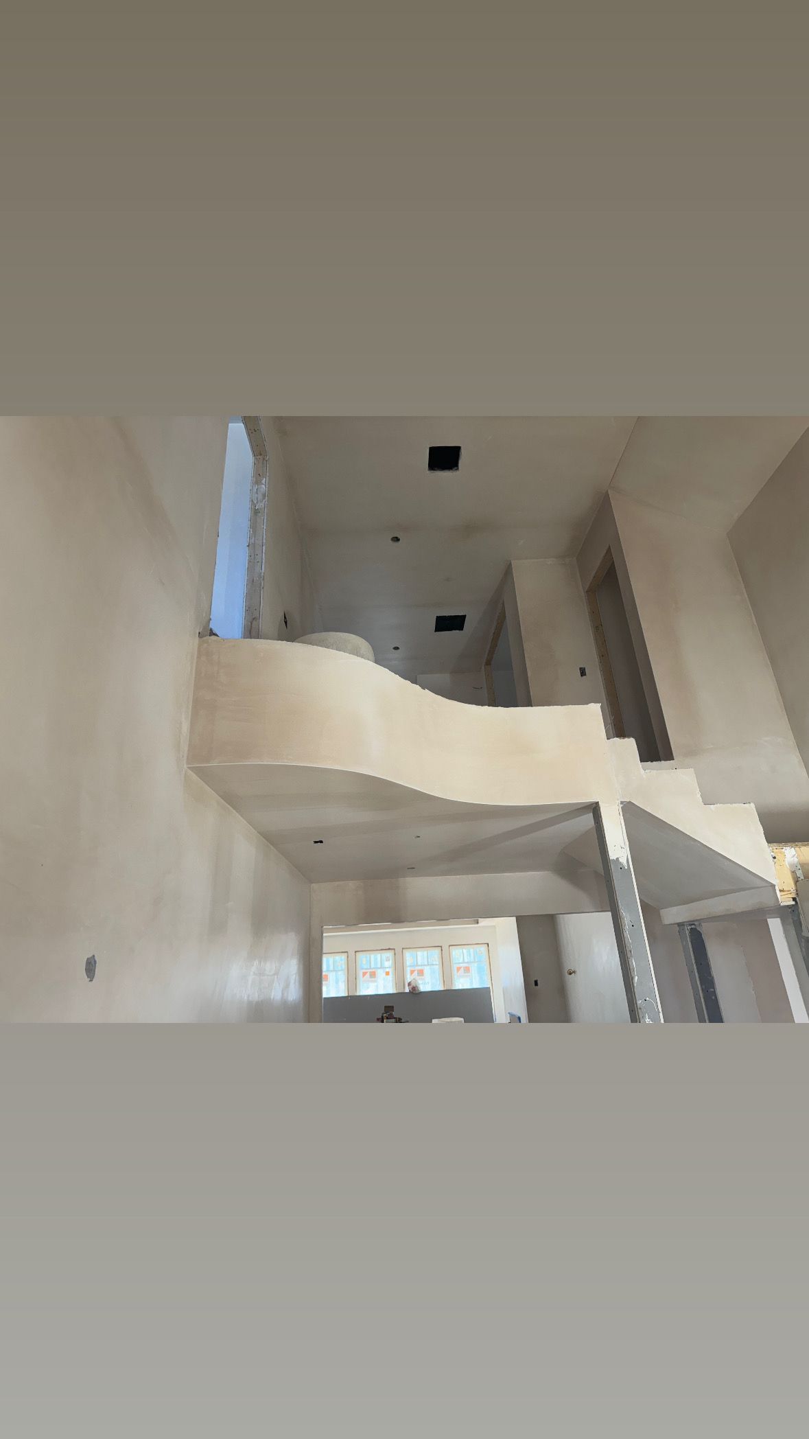 Interior of a modern unfinished stairwell with white walls, curved balcony, and windows below