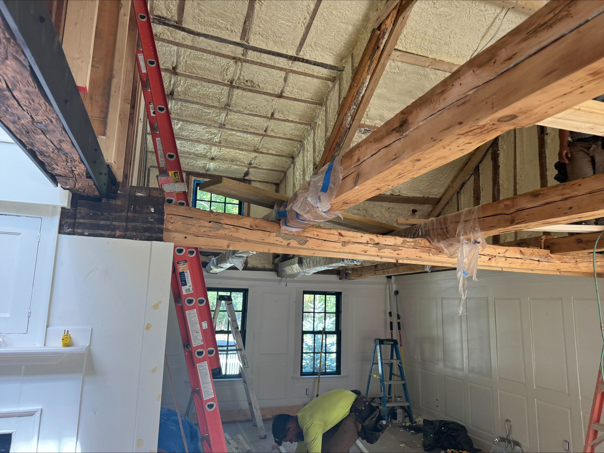 Wooden roof beams exposed during interior renovation, with a worker in a yellow shirt below.