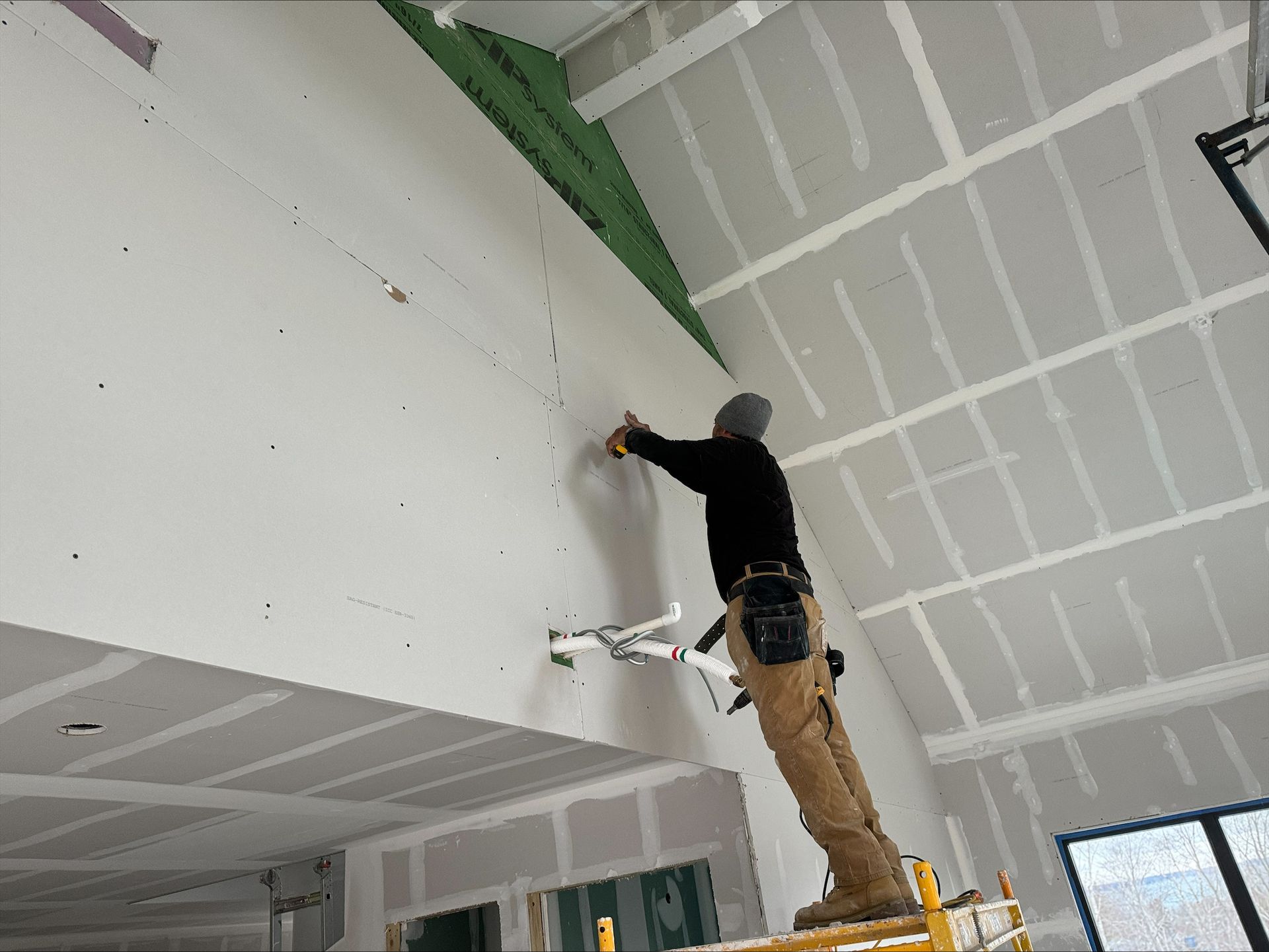 Worker on a ladder painting or patching a white ceiling in a room under construction.