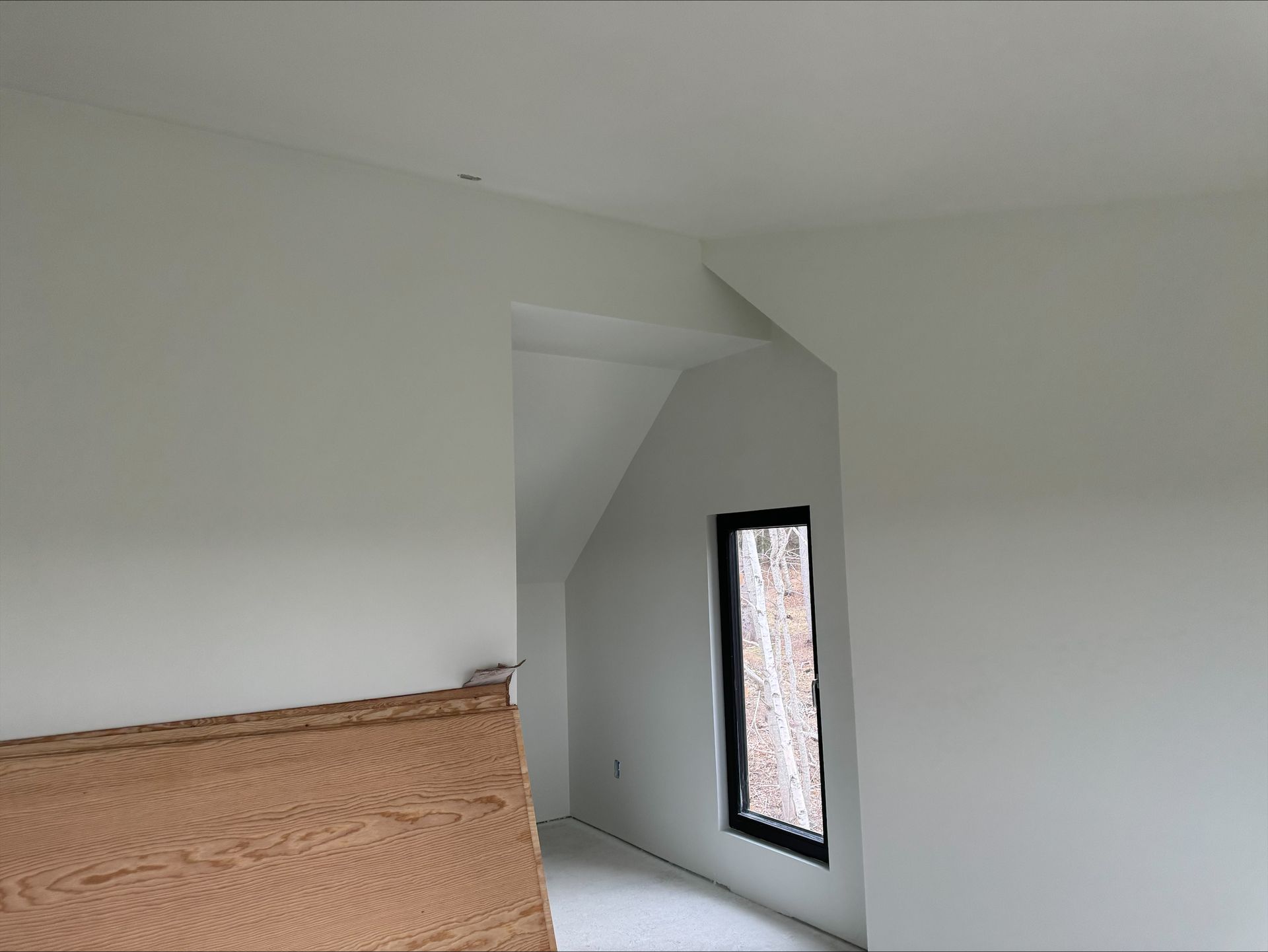 Empty white room with a slanted ceiling and a small narrow window beside a headboard.