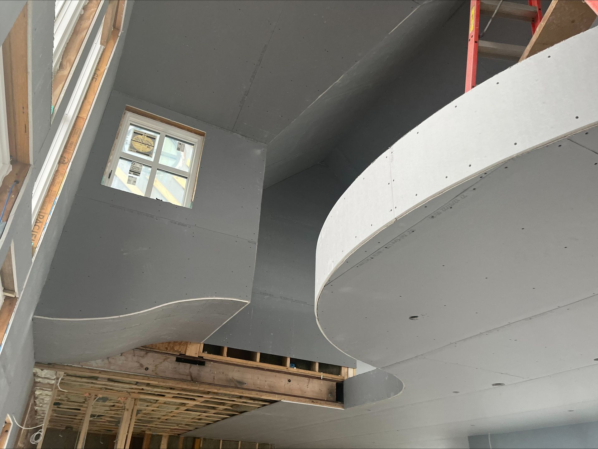 Interior of a building under construction, with a curved white staircase and exposed framing below.