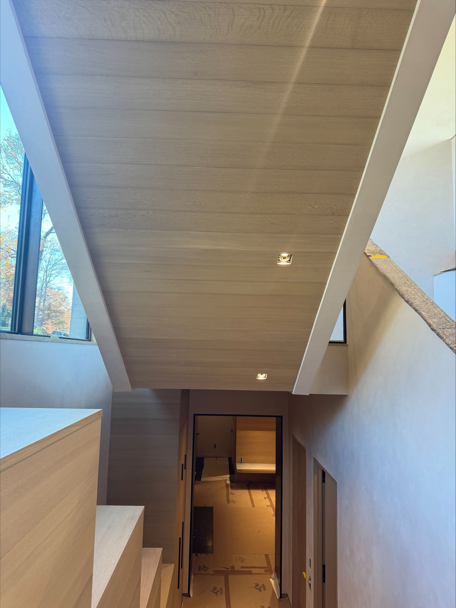 Modern interior stairwell with wood ceiling panels, white walls, and a view down to a lower floor hallway.