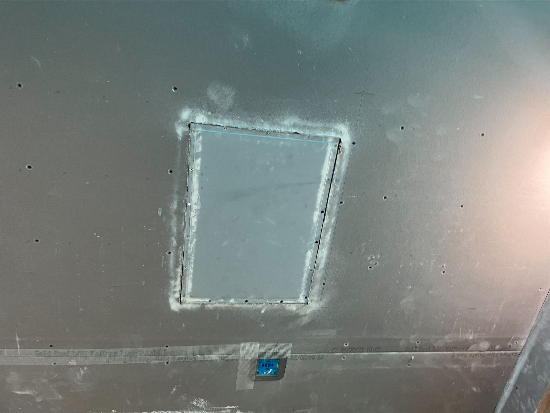 A gray ceiling with a rectangular access panel and a small blue vent or sensor below it.