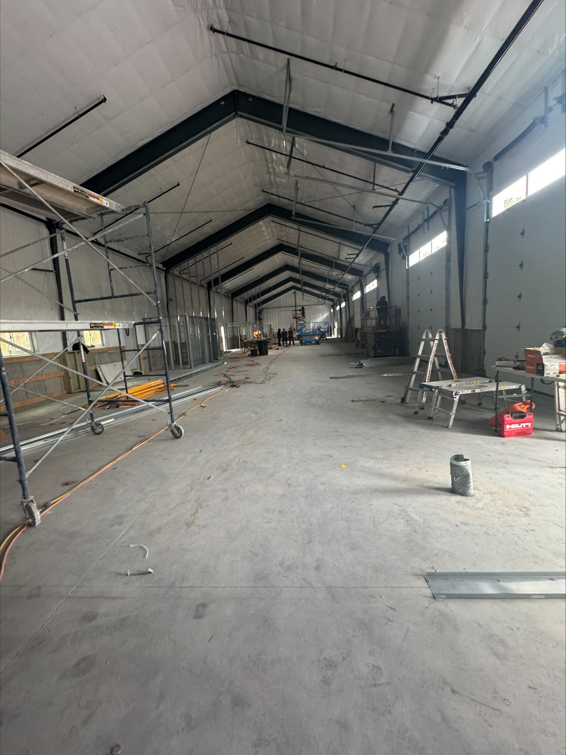 Empty industrial warehouse interior with metal scaffolding, ladders, and construction debris on the floor