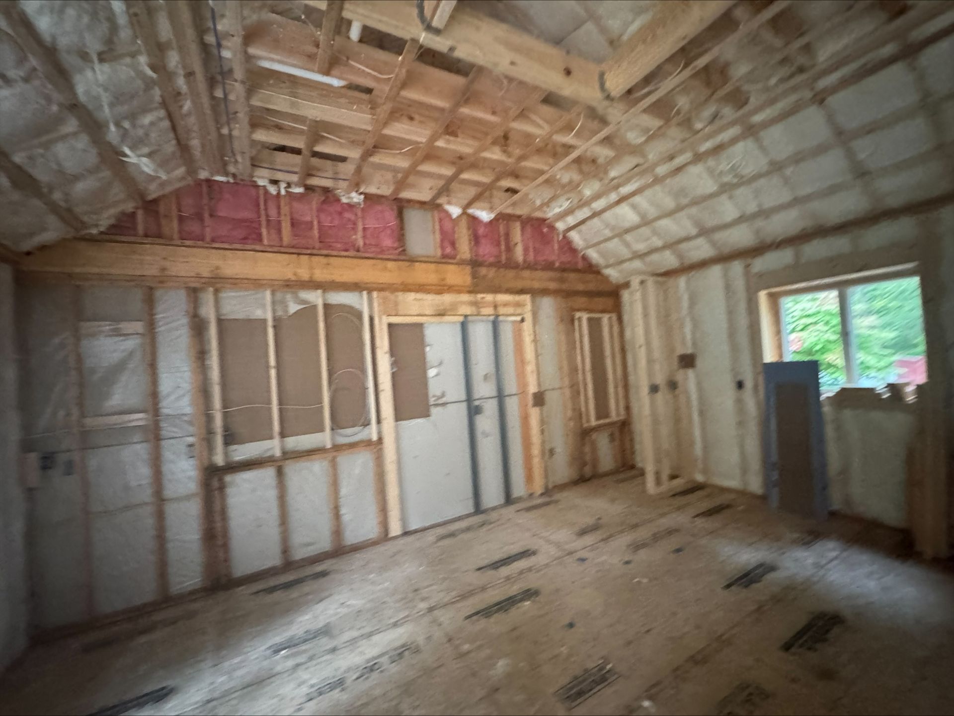 Unfinished room with exposed framing, insulation, and a window letting in daylight.