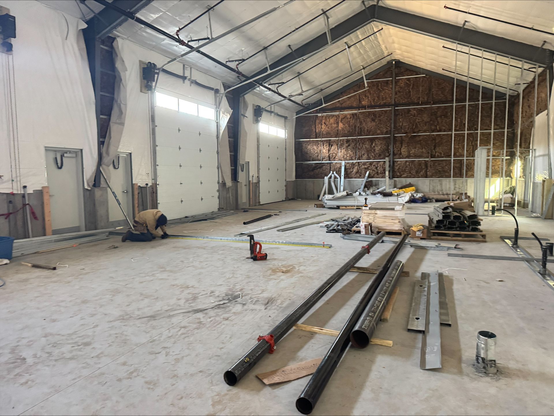 Empty warehouse under construction with metal beams, tools, and insulation on the far wall