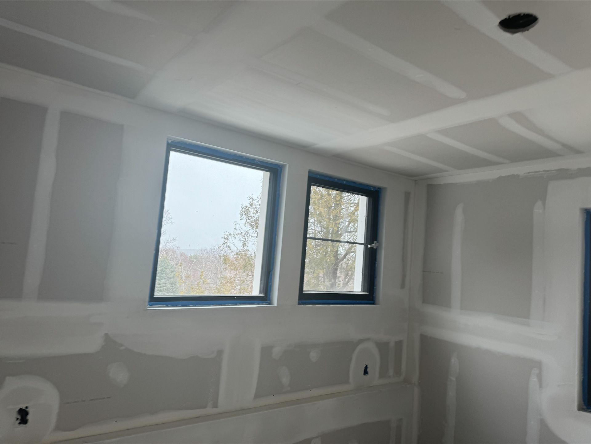 Unfinished room with drywall, two windows, and a white ceiling under construction.