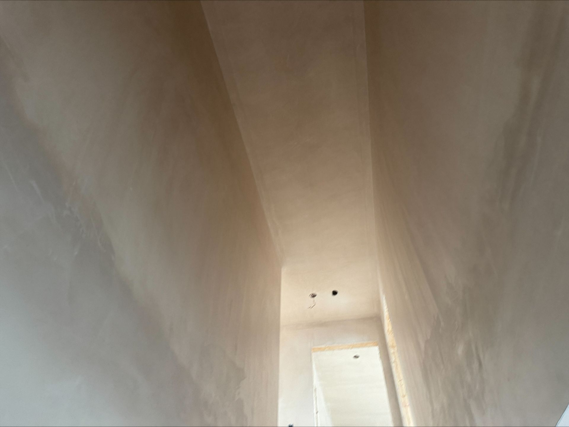 A narrow unfinished stairwell with white walls and a bright opening below.