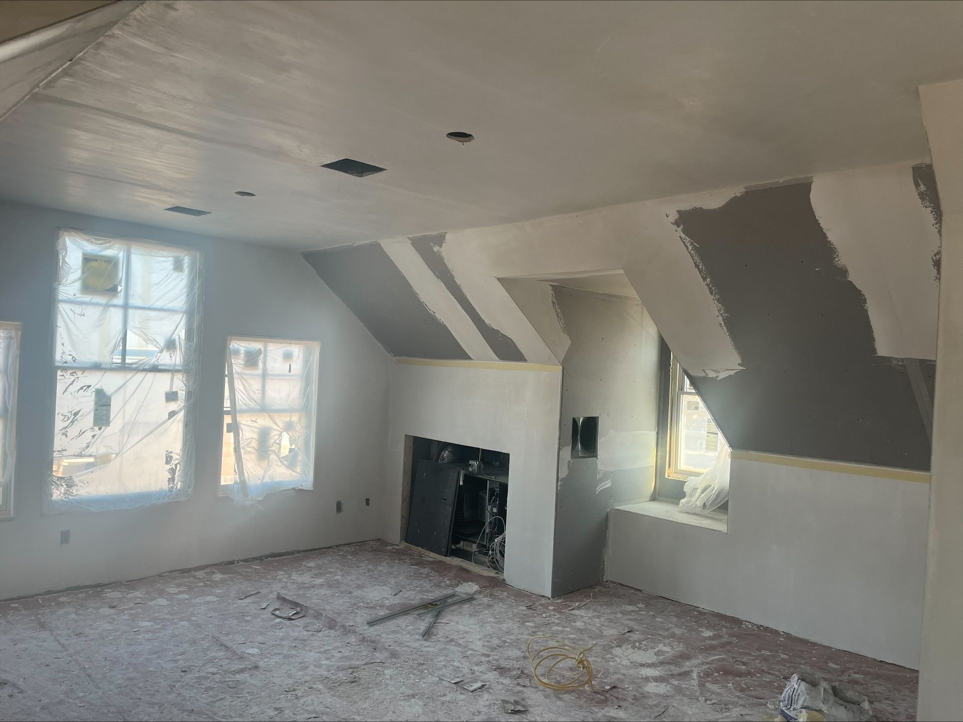 Renovated attic room with white walls, sloped ceiling, windows, and unfinished drywall patches