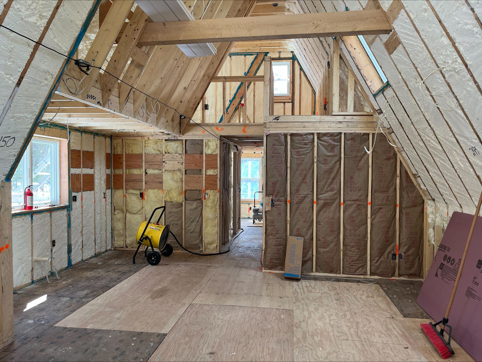Unfinished attic room under construction with exposed insulation, wooden framing, and tools on the floor.
