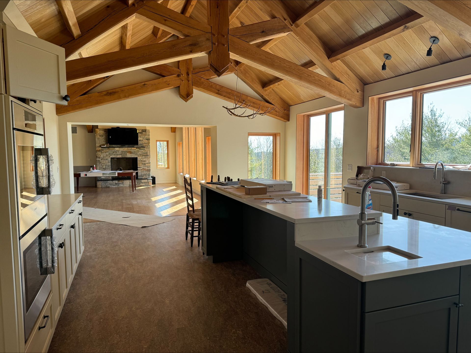 Modern open kitchen with wood beams, dark cabinets, and large windows in a bright rustic home