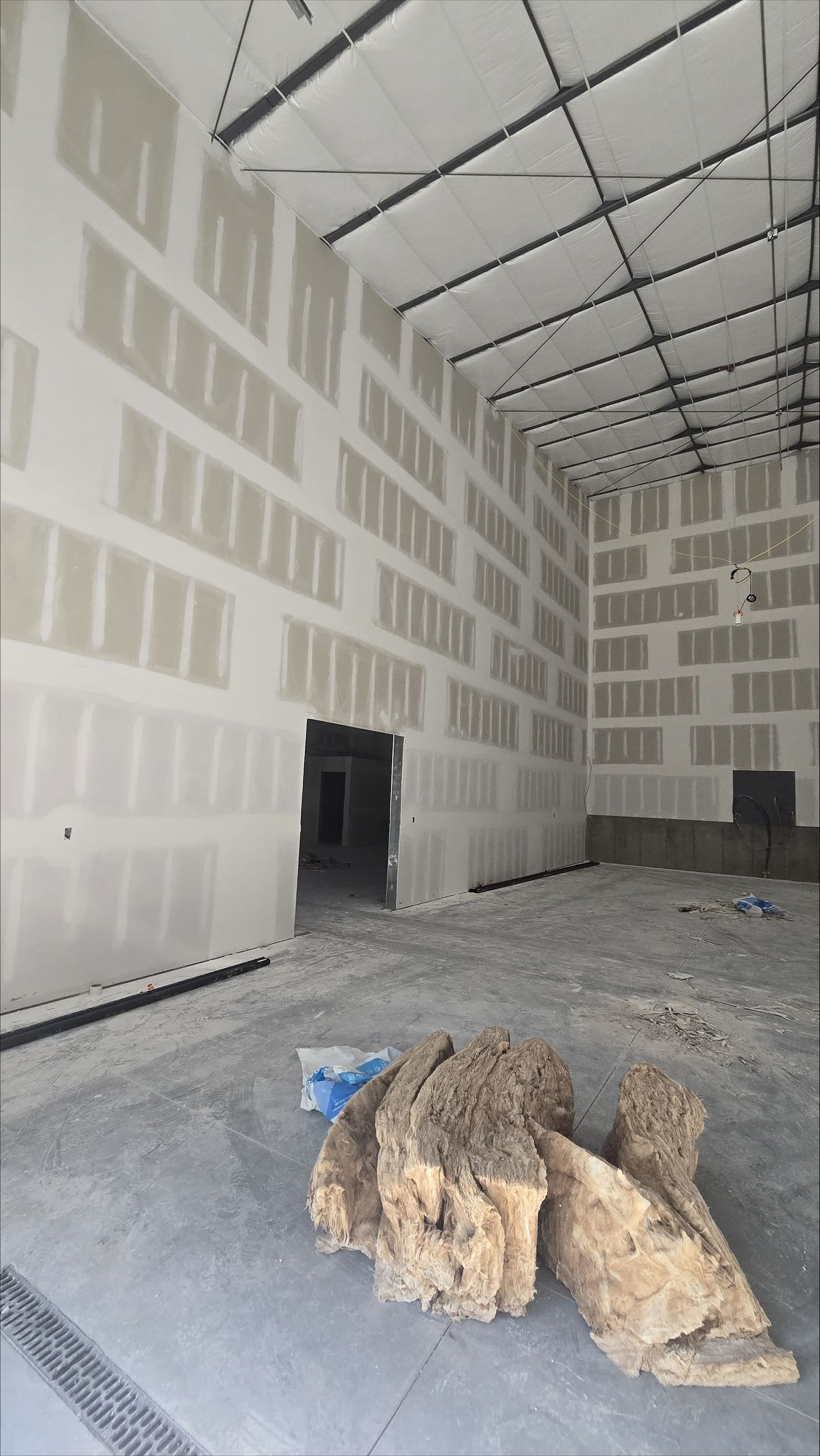 Empty unfinished warehouse interior with drywall, high ceiling, and debris on the floor