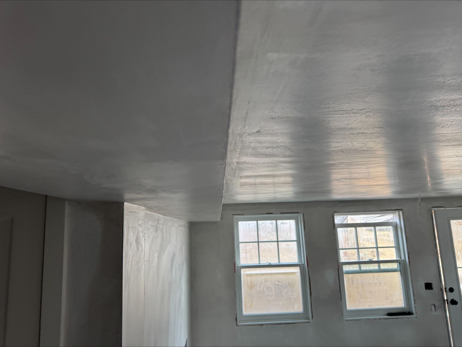 White-painted room interior with a low ceiling, three windows, and a glass door.