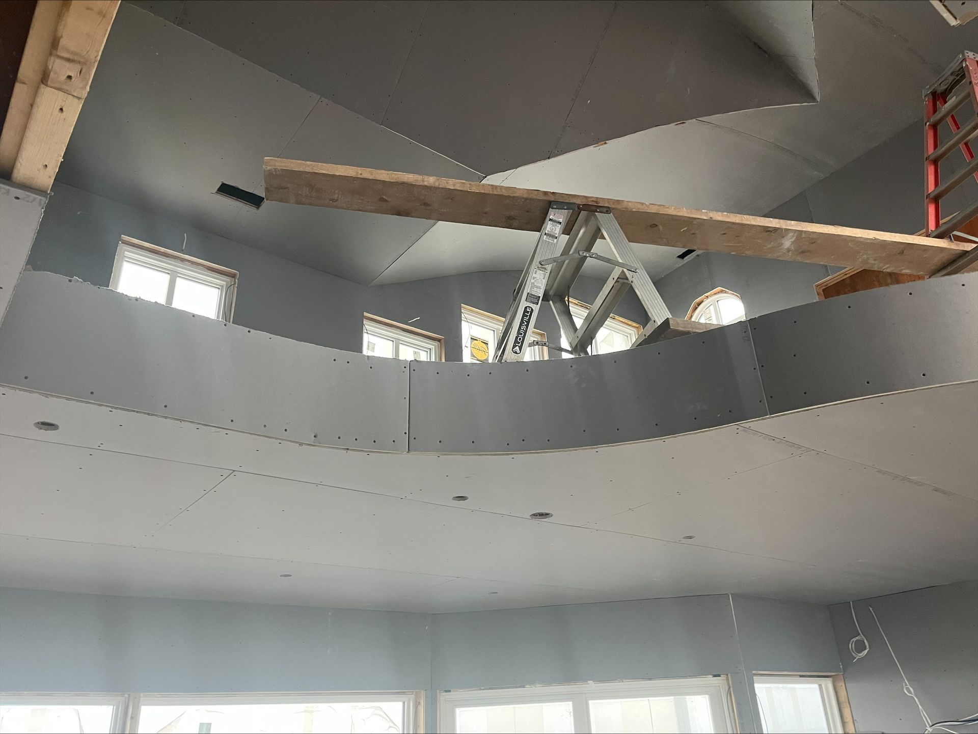 Interior of a building under construction with a wooden beam on a metal scaffold and curved gray walls.