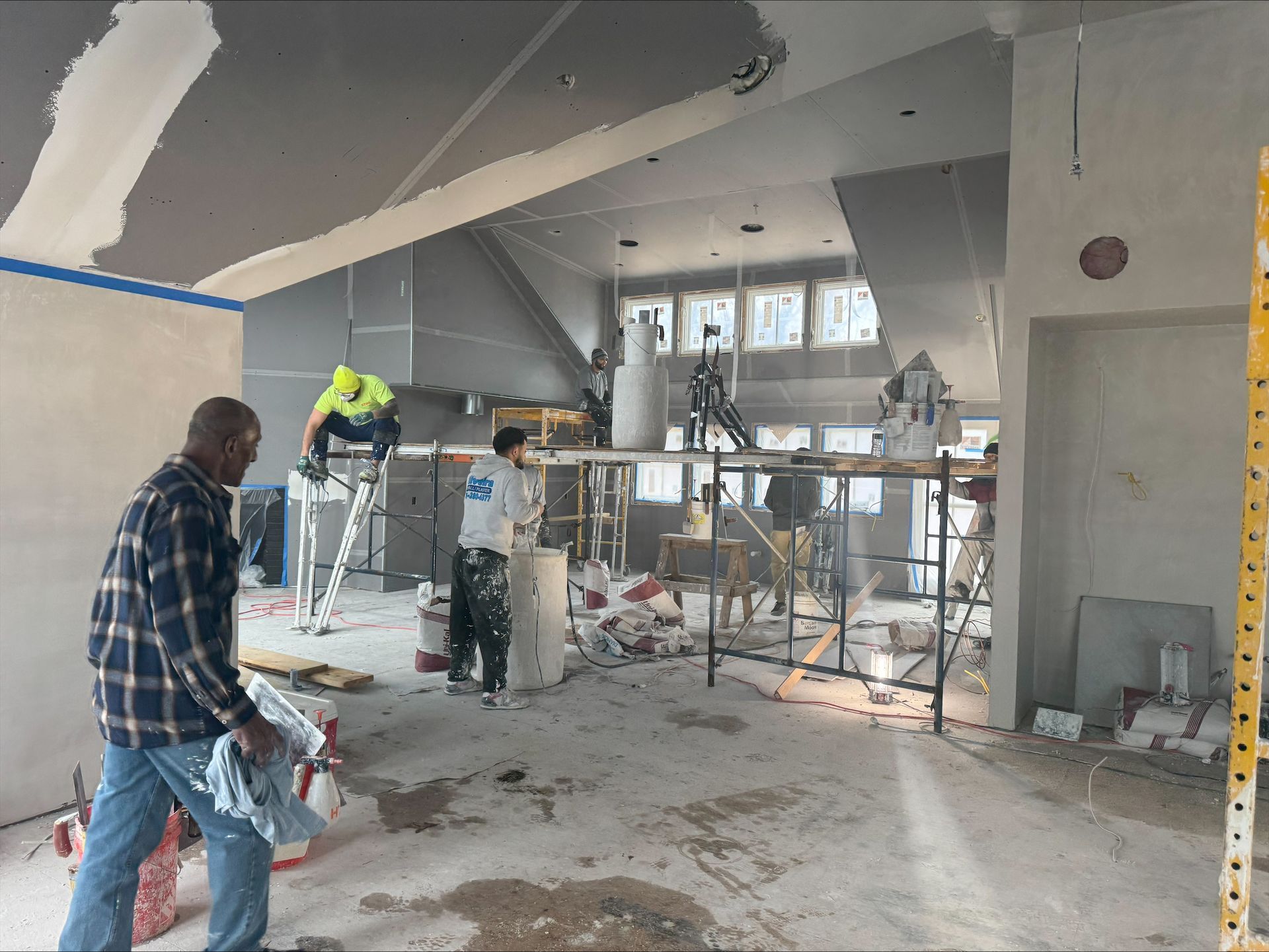 Workers renovating a damaged room with scaffolding, tools, and debris on the floor
