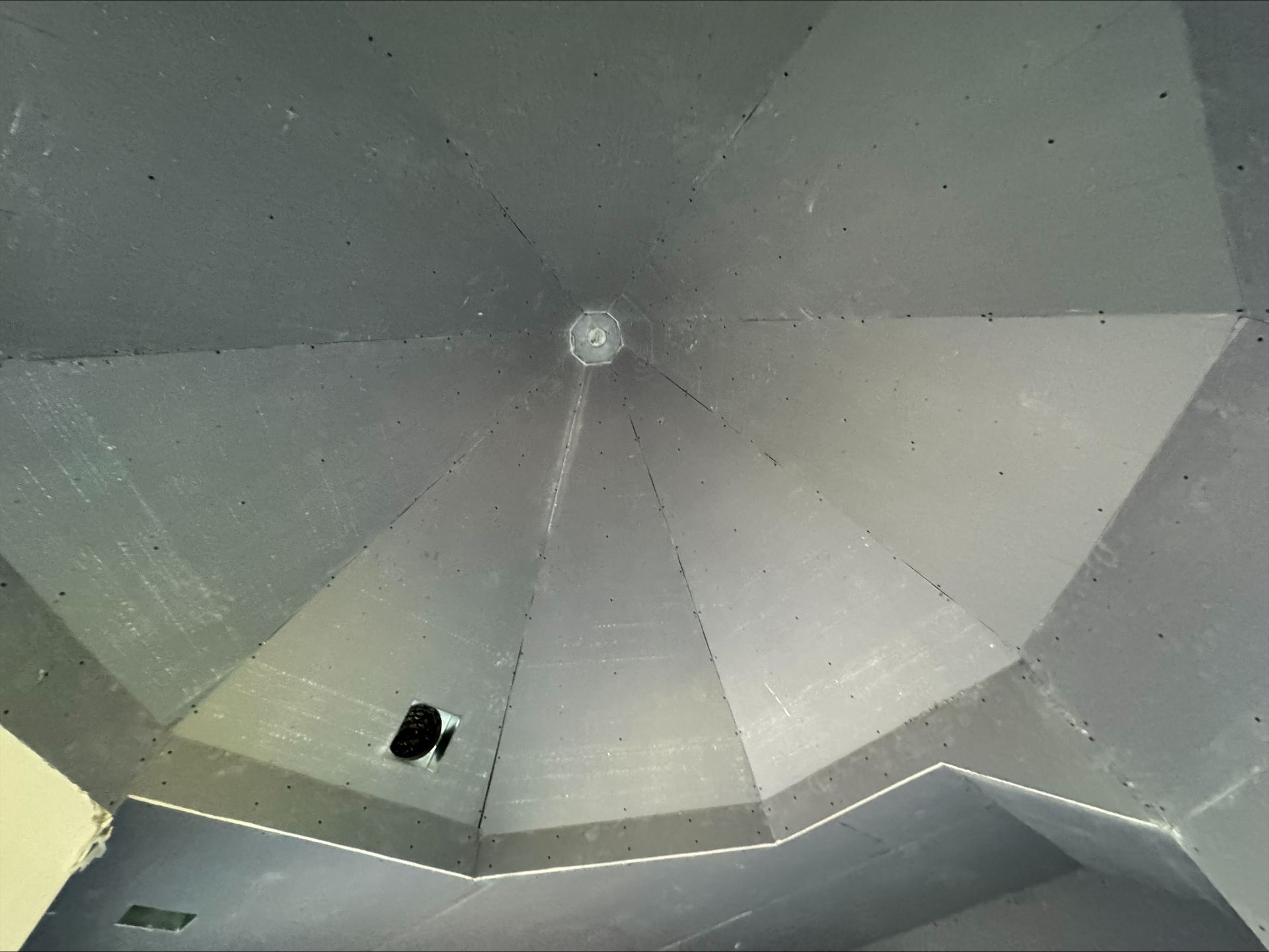 Gray tent ceiling with central pole and small black object near one panel seam