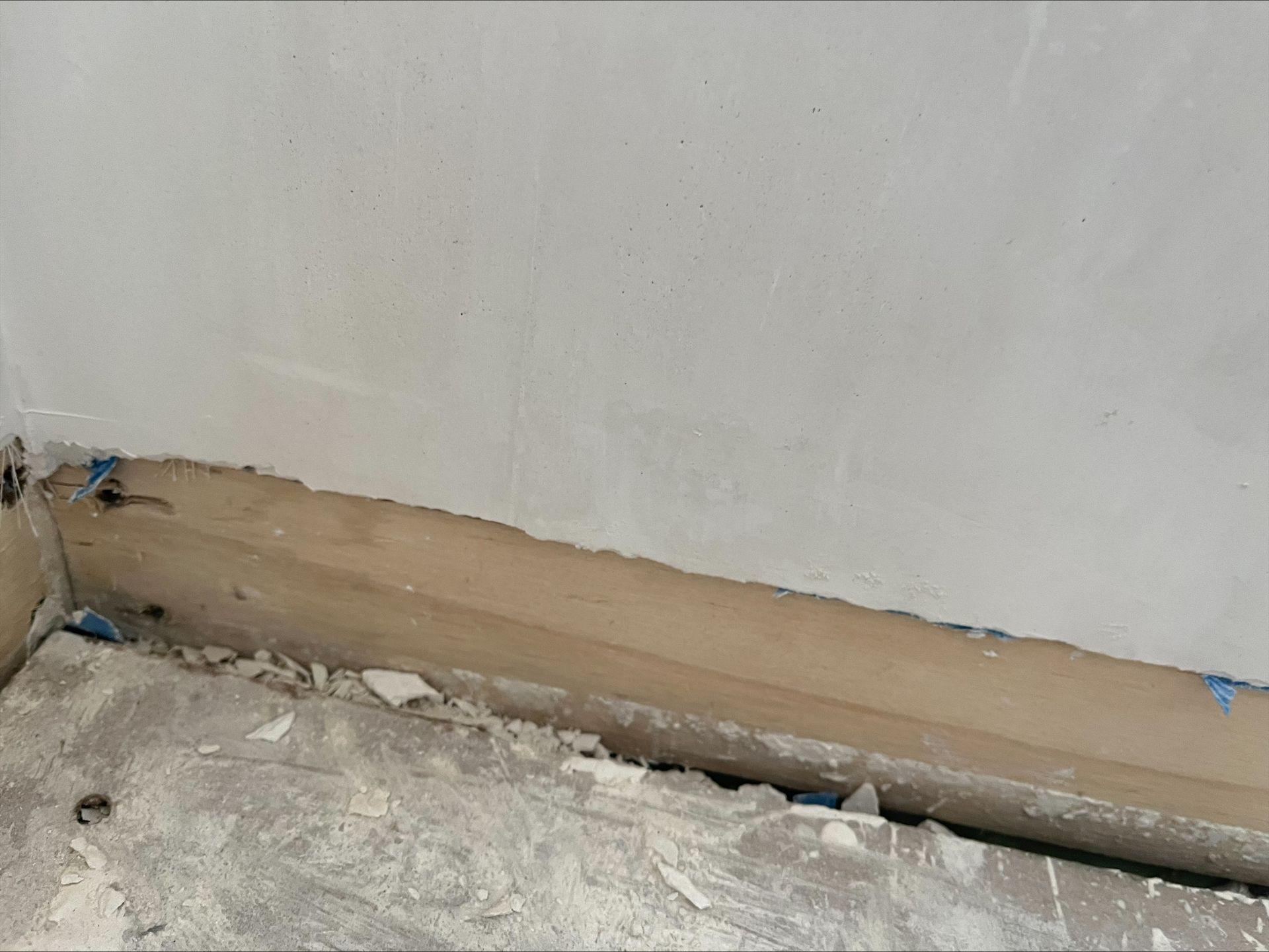 Partially painted wall with a stained baseboard and debris on the floor during renovation