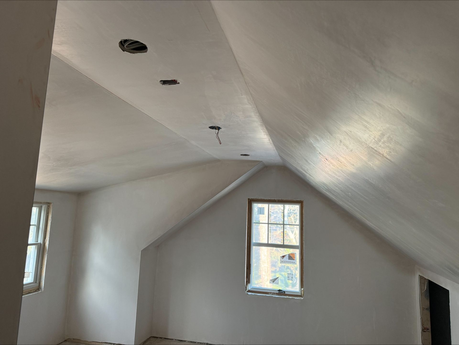 Empty white attic room with sloped ceiling, recessed lights, and a small window