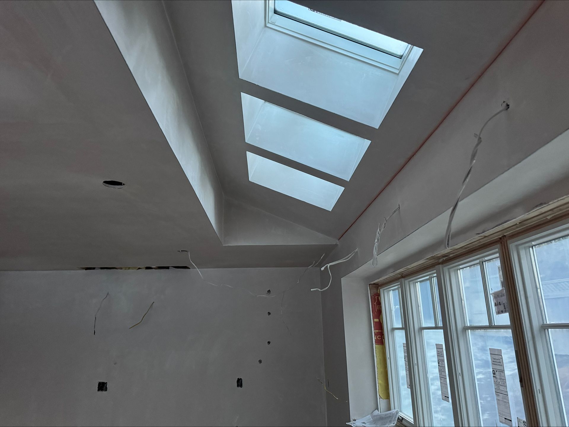Bright room interior with slanted skylights, white ceiling, and large windows under renovation.