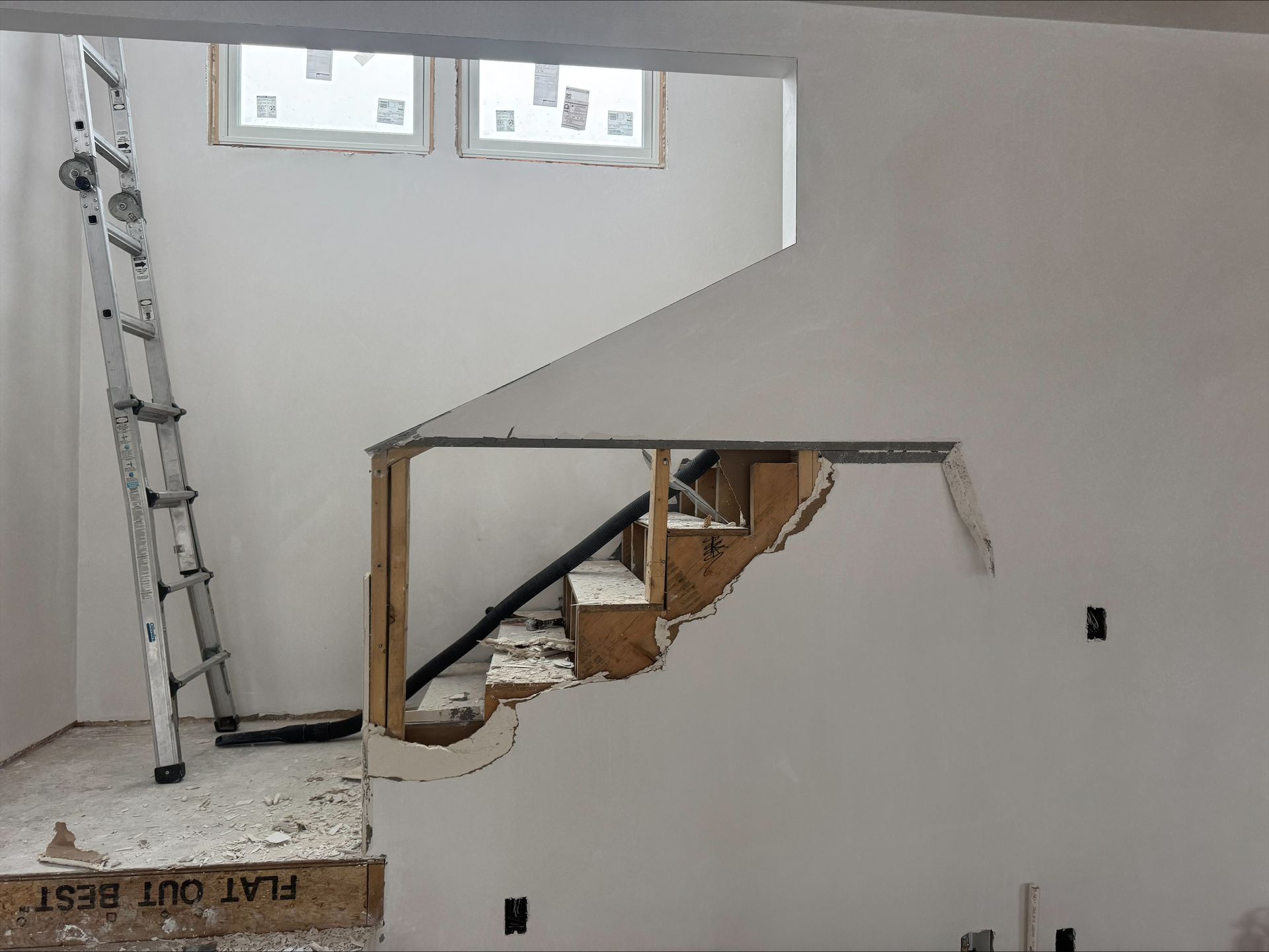 Interior under construction with open staircase, exposed wood framing, and a ladder against the wall.