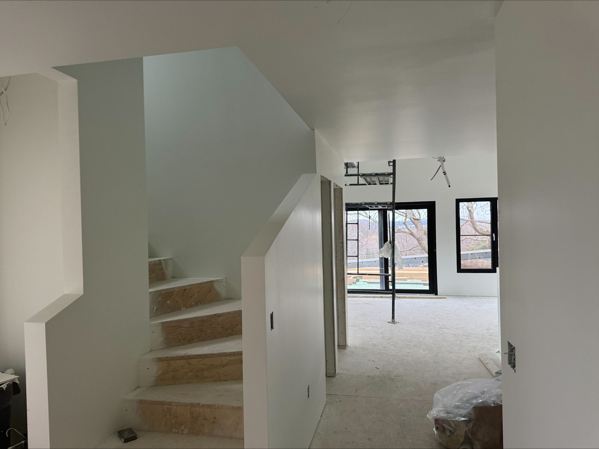 Empty house interior with unfinished staircase and carpeted hallway leading to glass doors