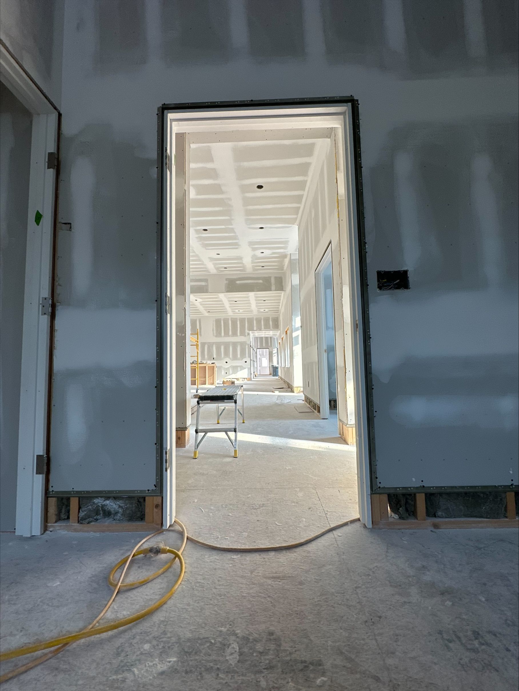 Unfinished interior doorway framing a bright hallway with construction materials and a yellow cable on the floor