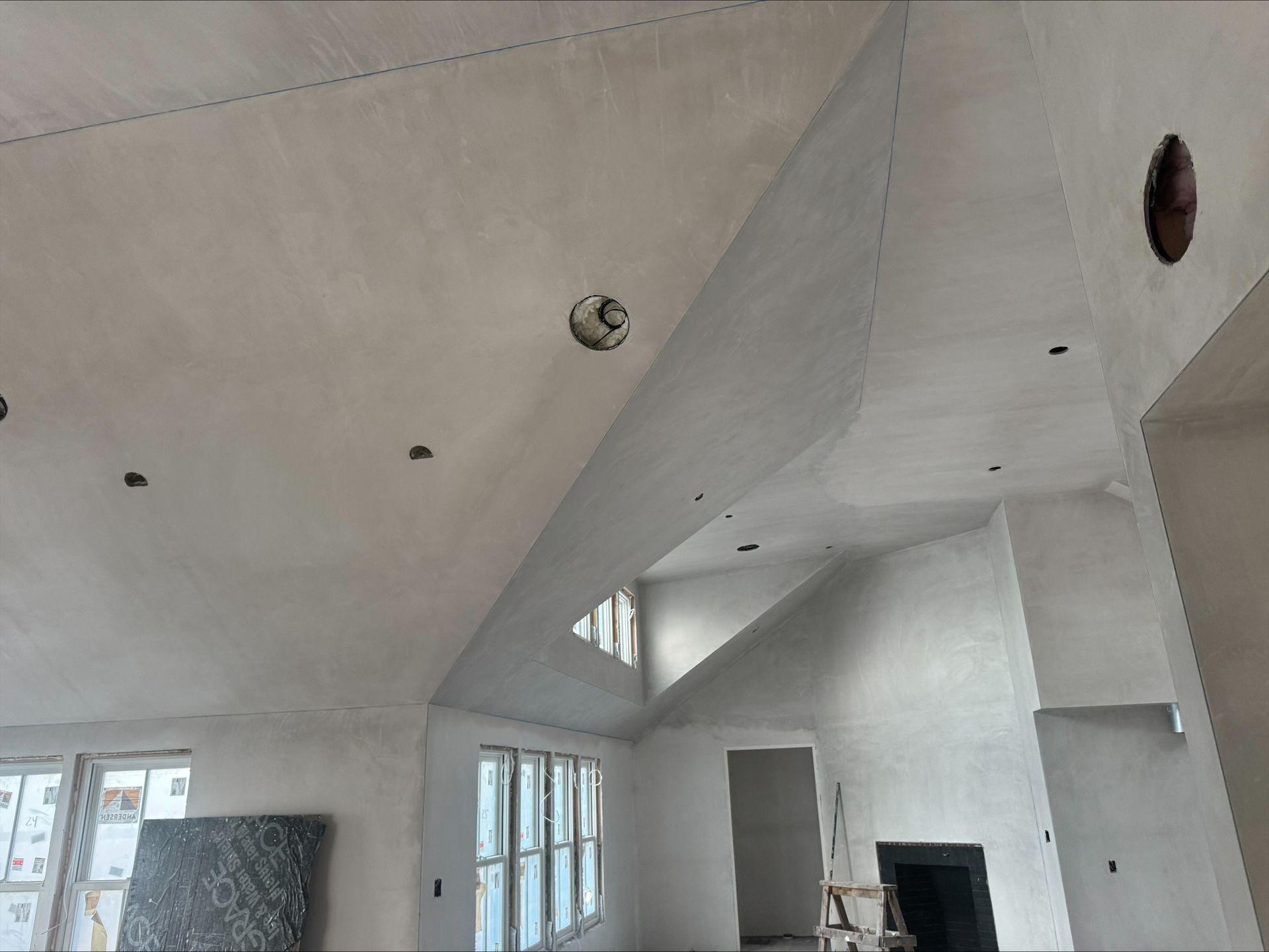 White modern living room with high vaulted ceiling, recessed lights, and a fireplace under construction