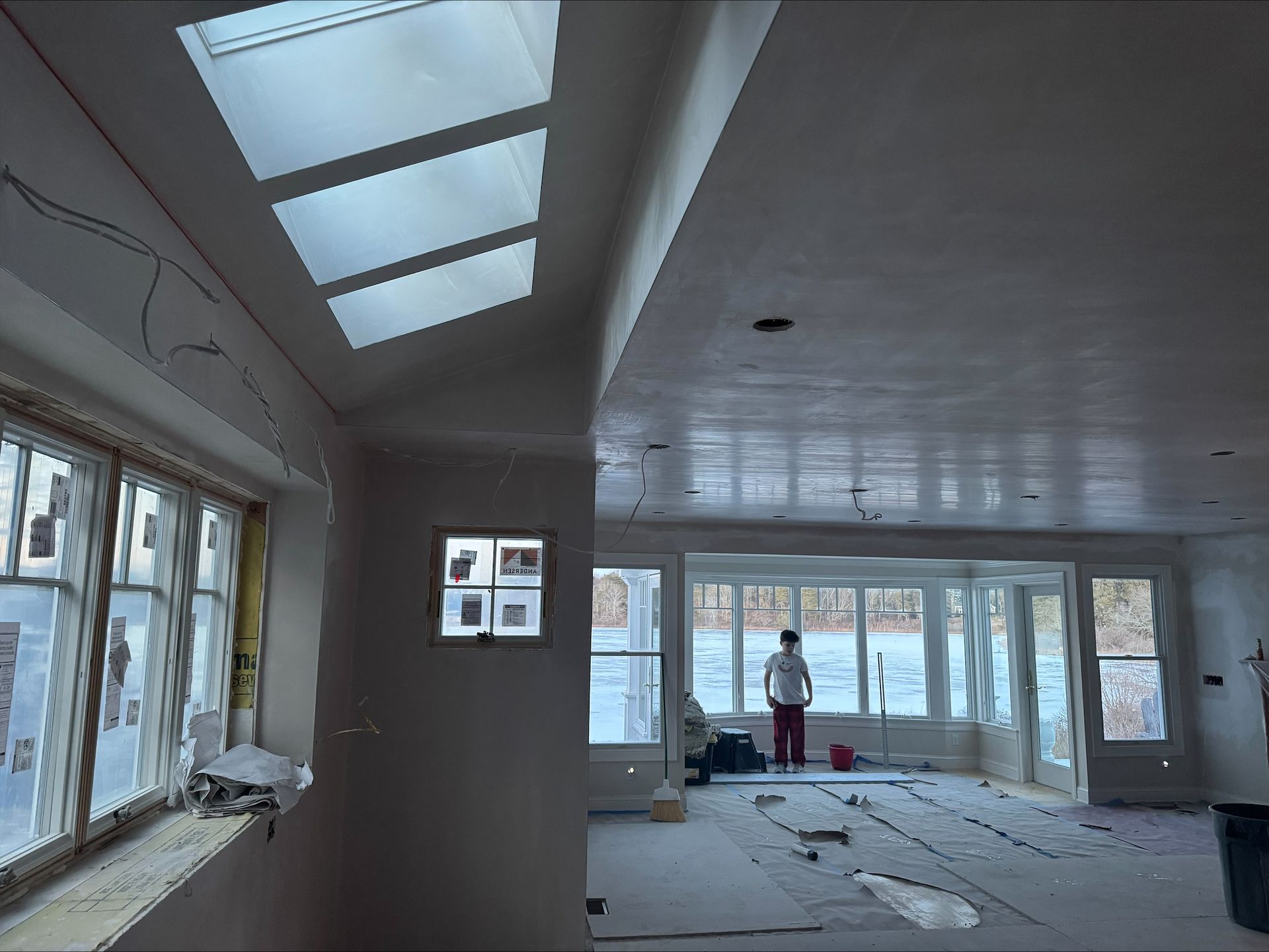 Empty room under renovation with skylights, unfinished floor, and a person standing near the far wall