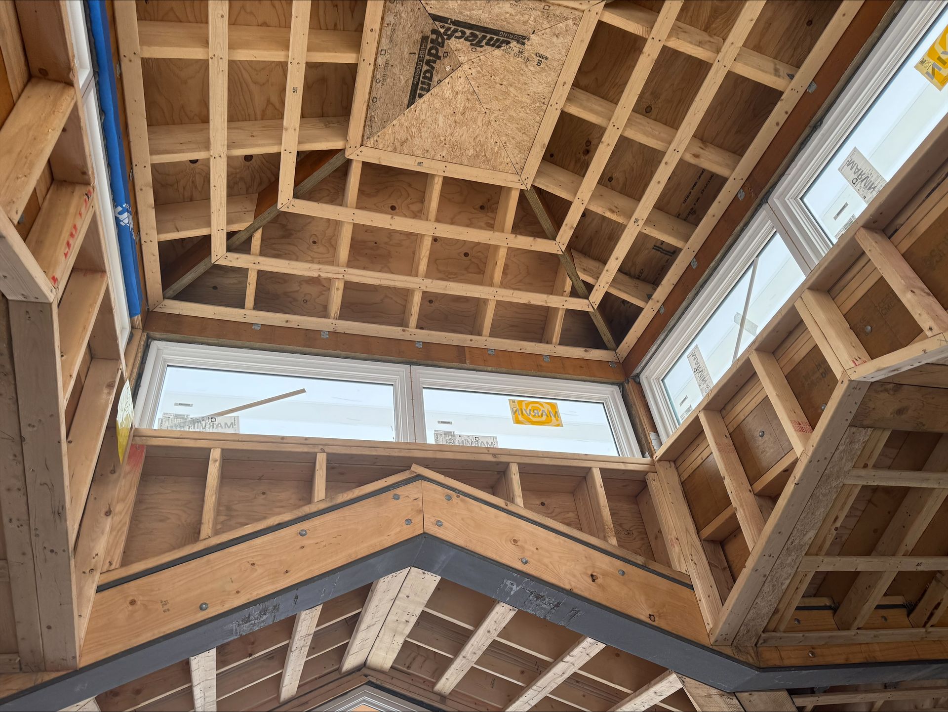 Interior framing of a house under construction, with exposed wooden roof trusses and wall studs.