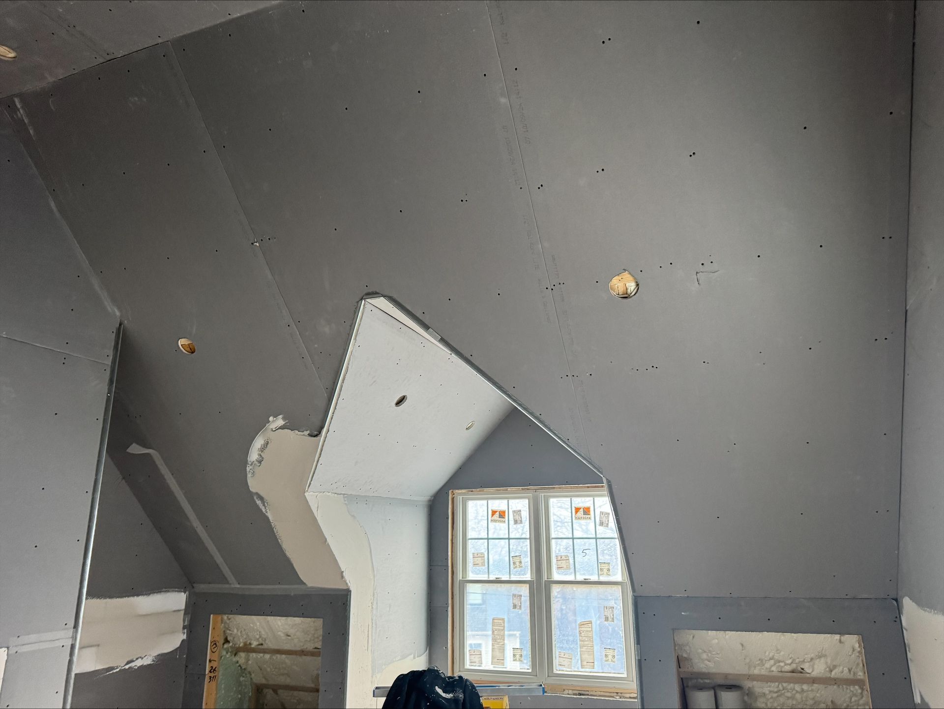 Partially finished room with dark gray walls, a slanted ceiling, and a window centered below a roof opening.