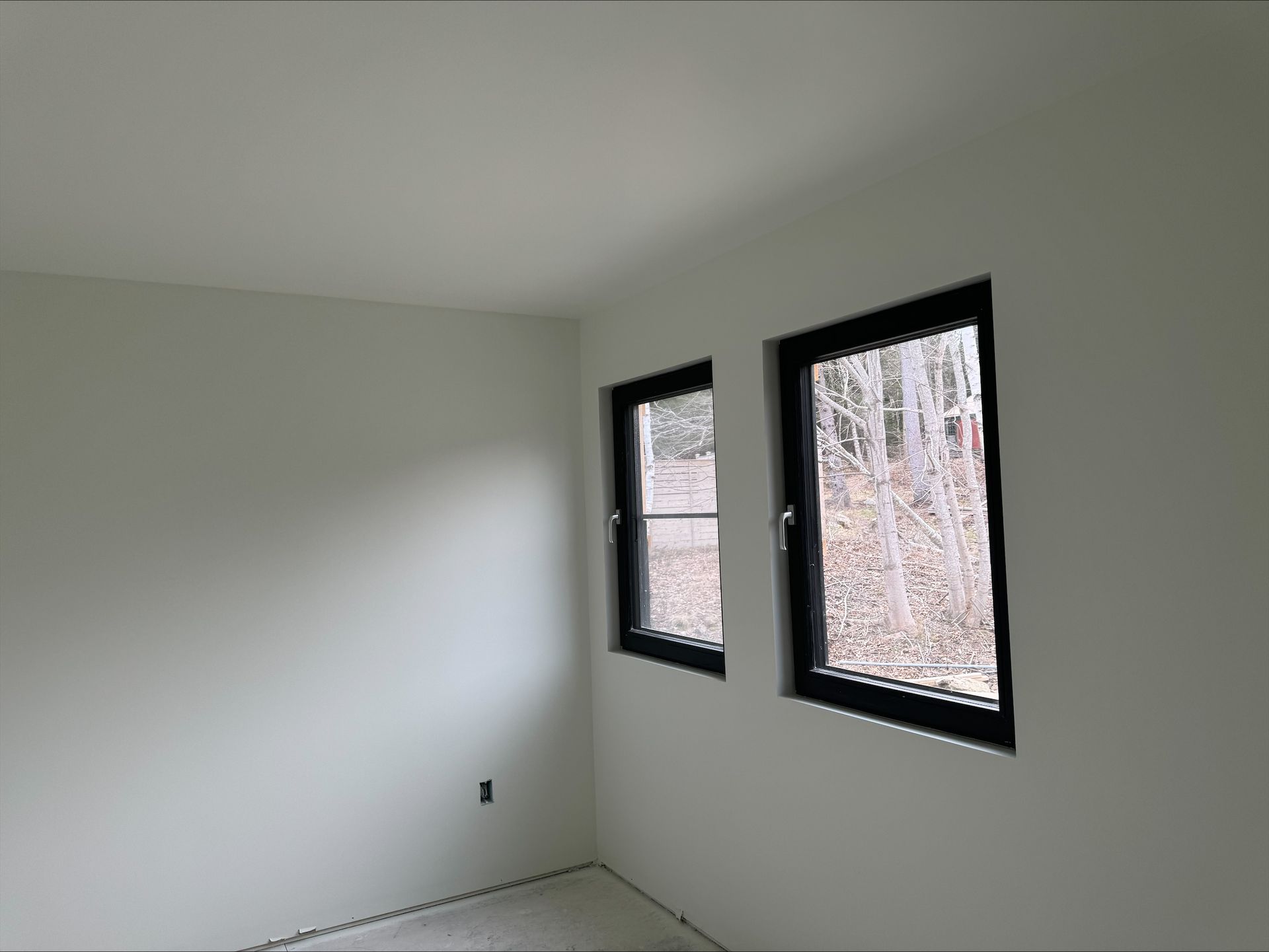 Empty white room with two black-framed windows and bare floor