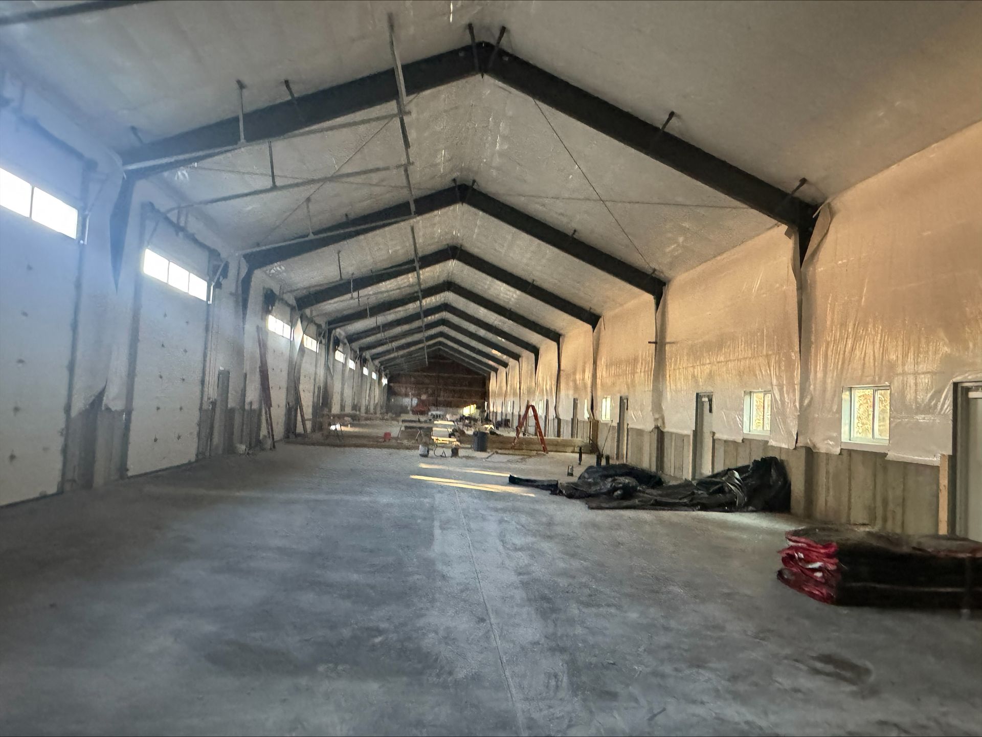 Empty industrial hall with concrete floor, high peaked ceiling, and scattered materials along the sides