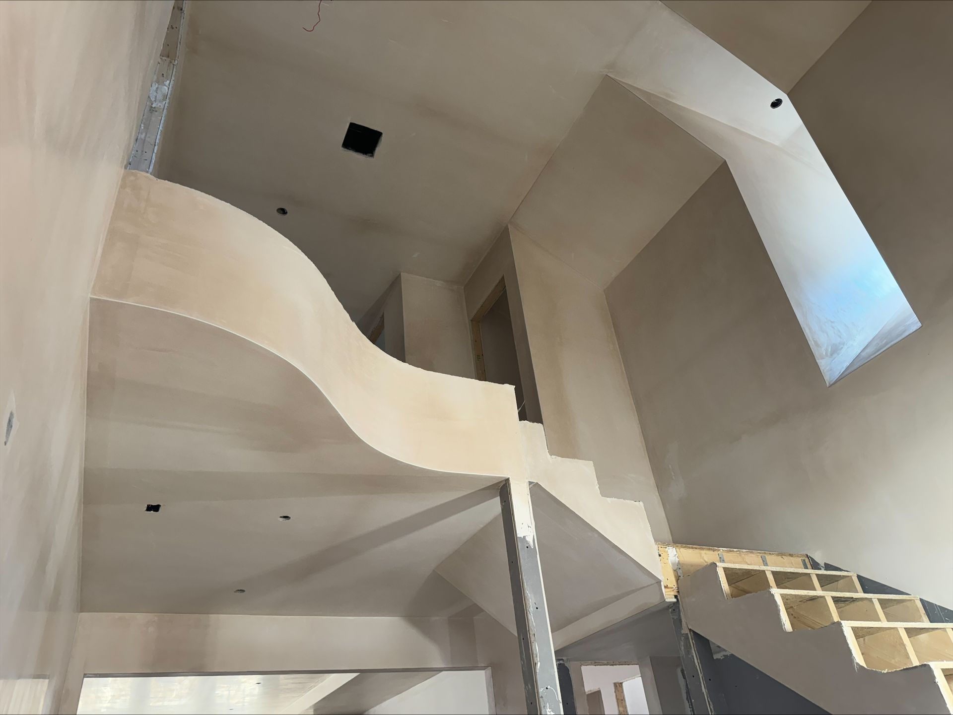 Interior of a modern stairwell with curving white walls and a small wooden staircase.
