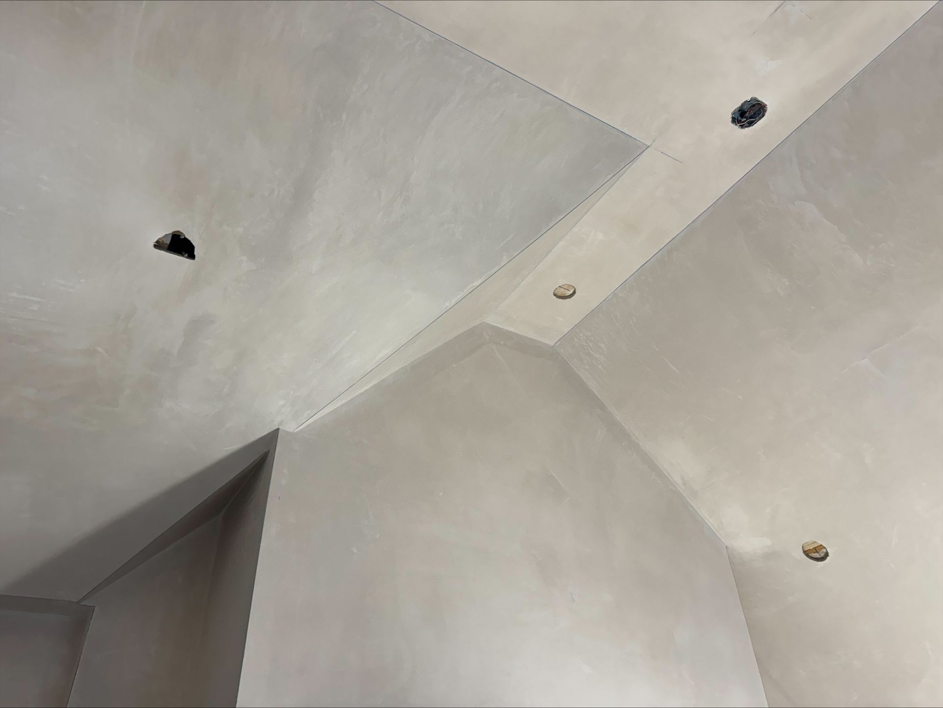 Ceiling corner with gray plaster, recessed lights, and a doorway edge