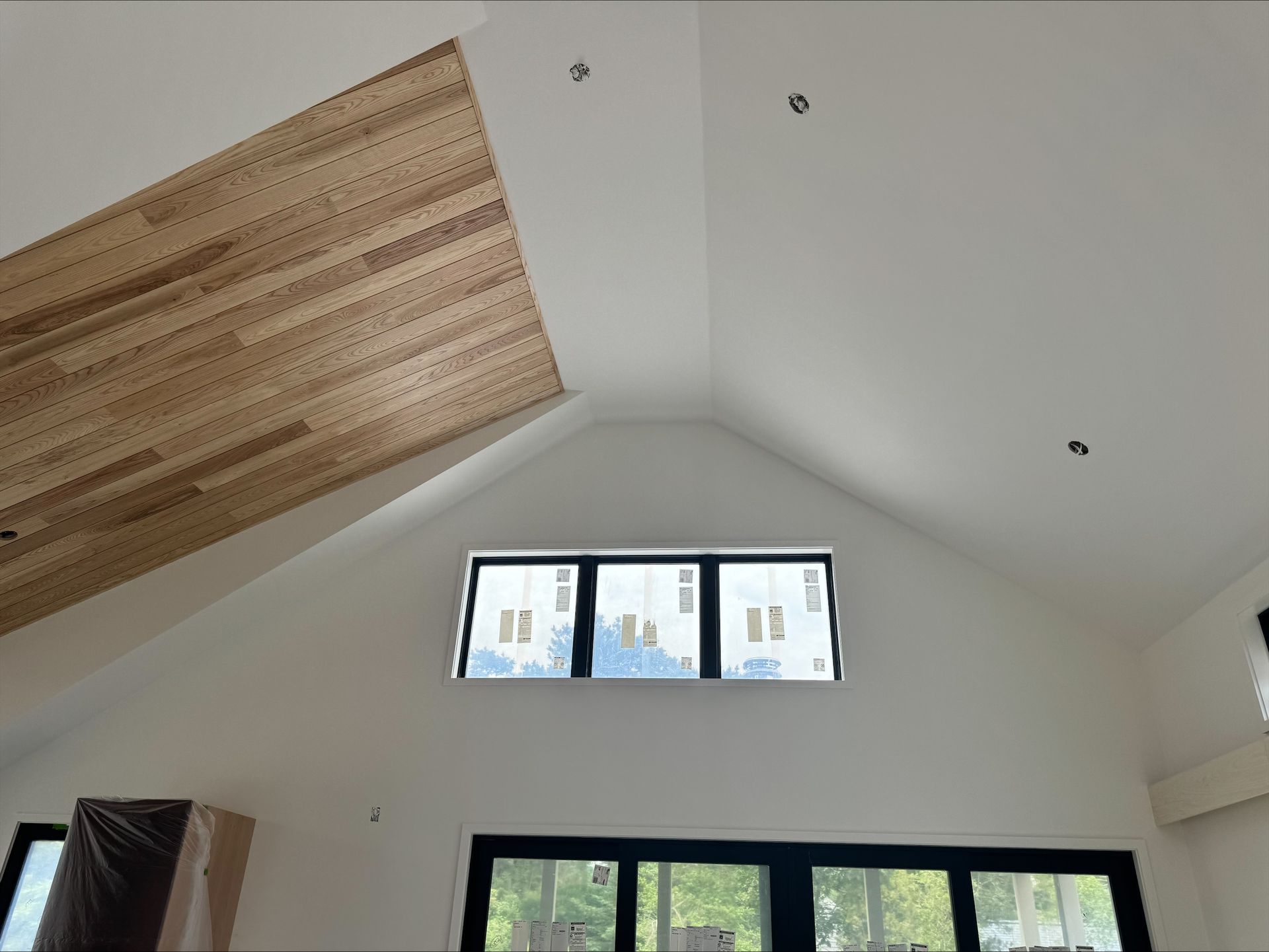 Interior with vaulted white ceiling, wood panel accent, and two black-framed windows above a doorway.