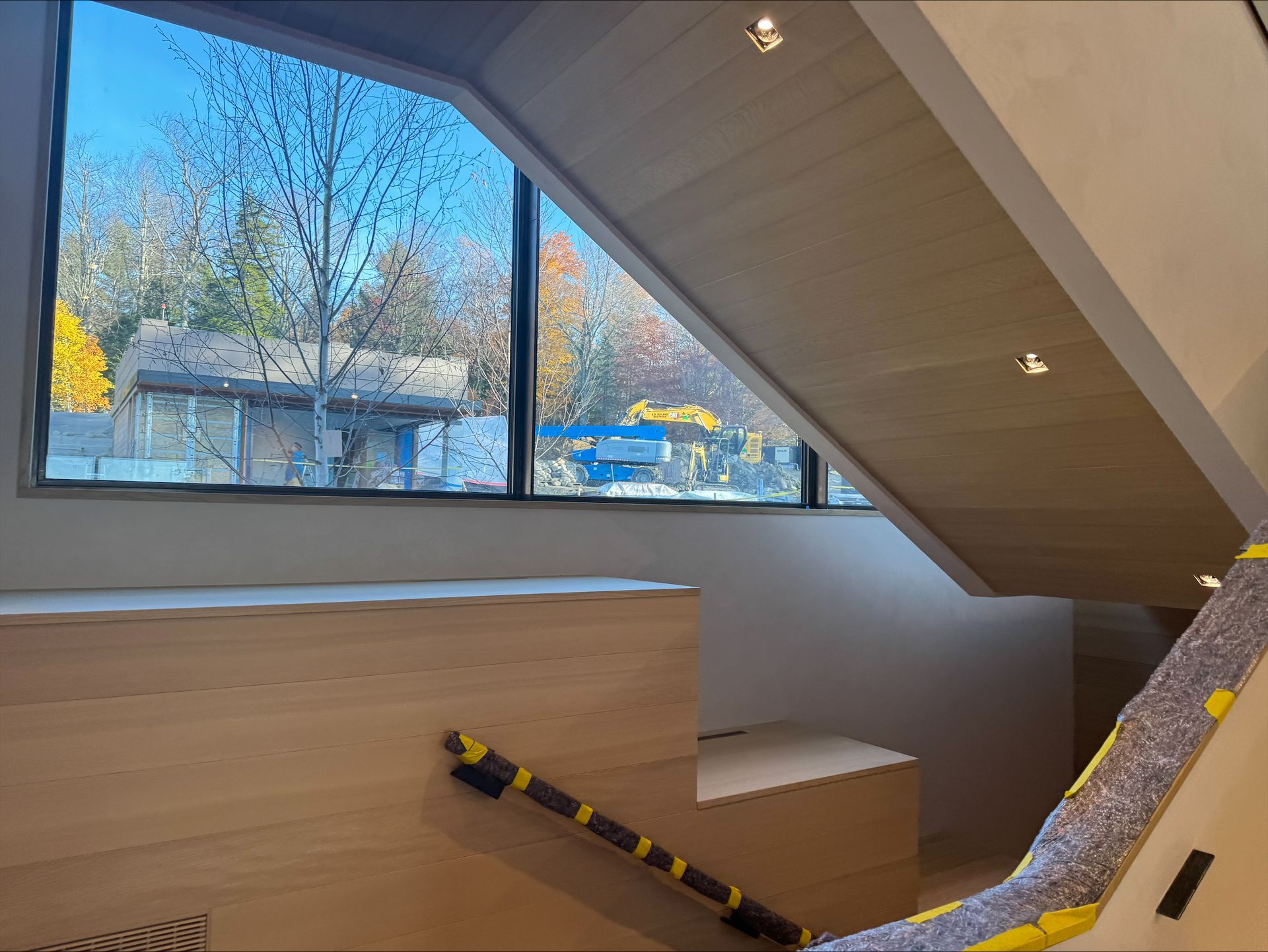 Modern attic interior with a large window, wood staircase, and yellow-black caution tape near the steps