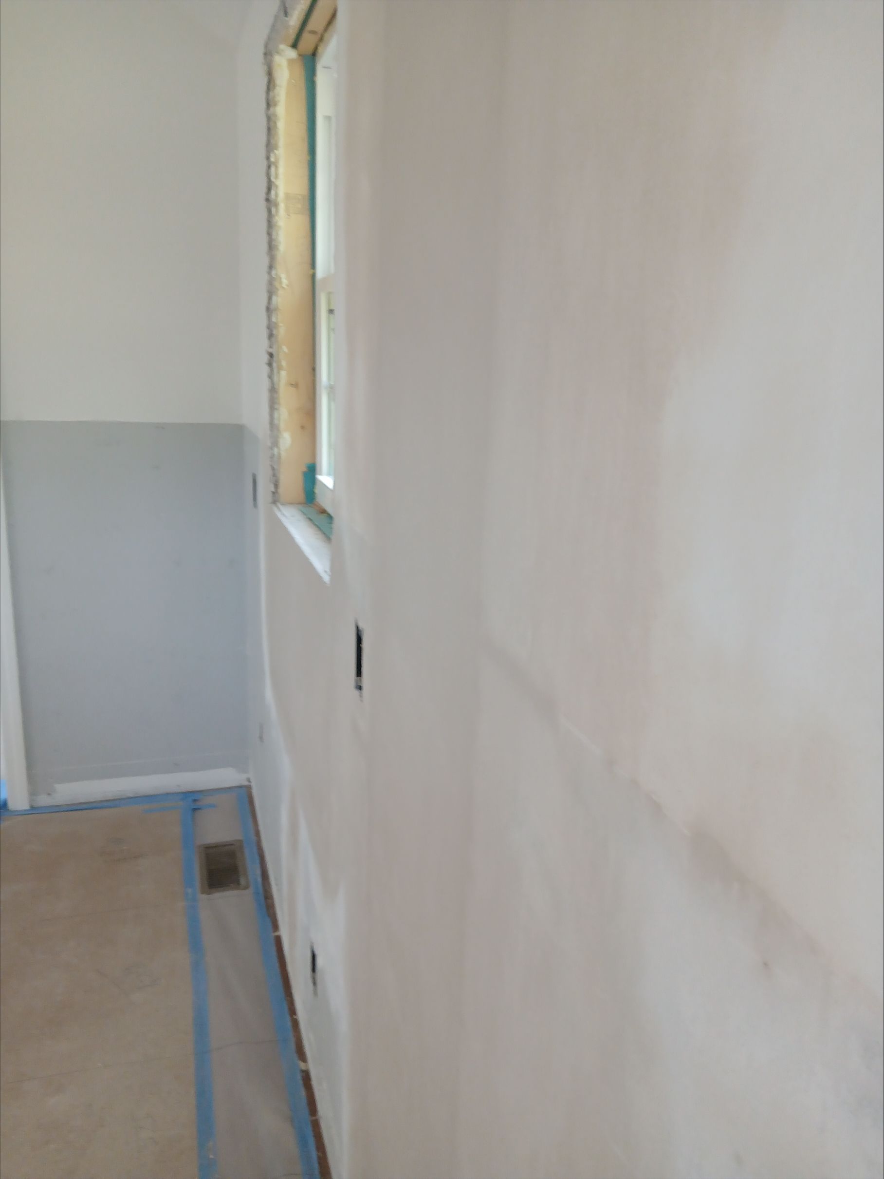 Empty room under renovation with white walls, window, and painter’s tape along the floor and baseboards