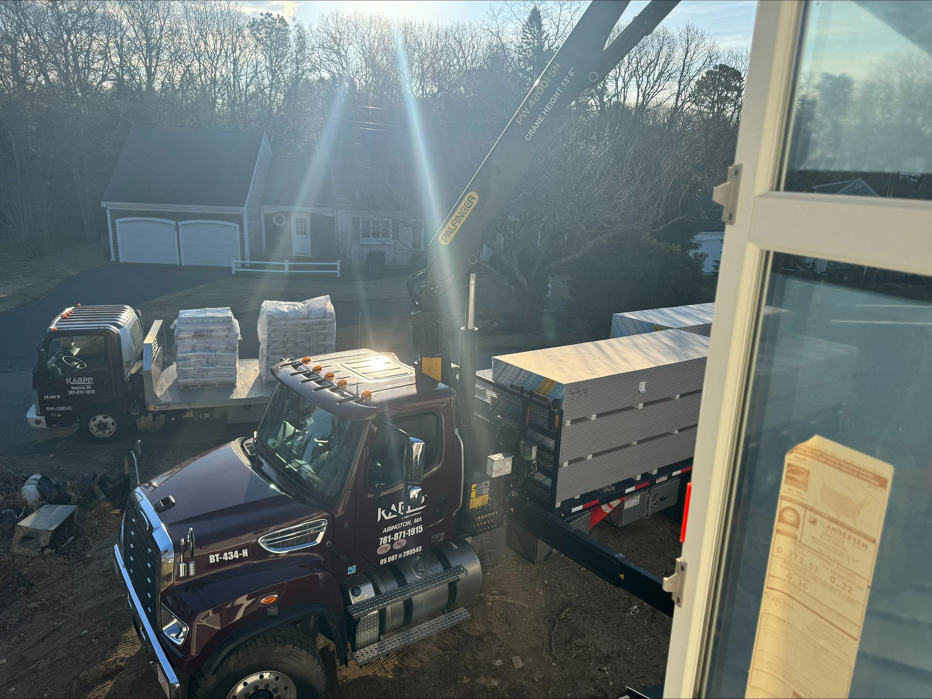 Tow truck hauling a white box truck in bright sunlight beside a window