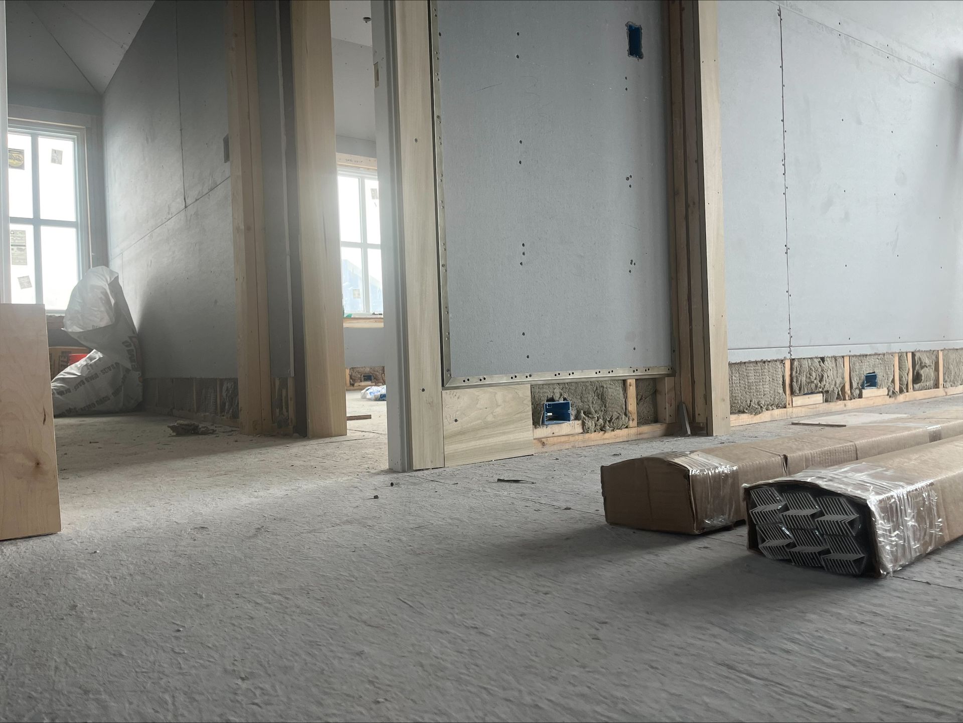 Unfinished room under construction with bare walls, exposed framing, and scattered materials on the floor