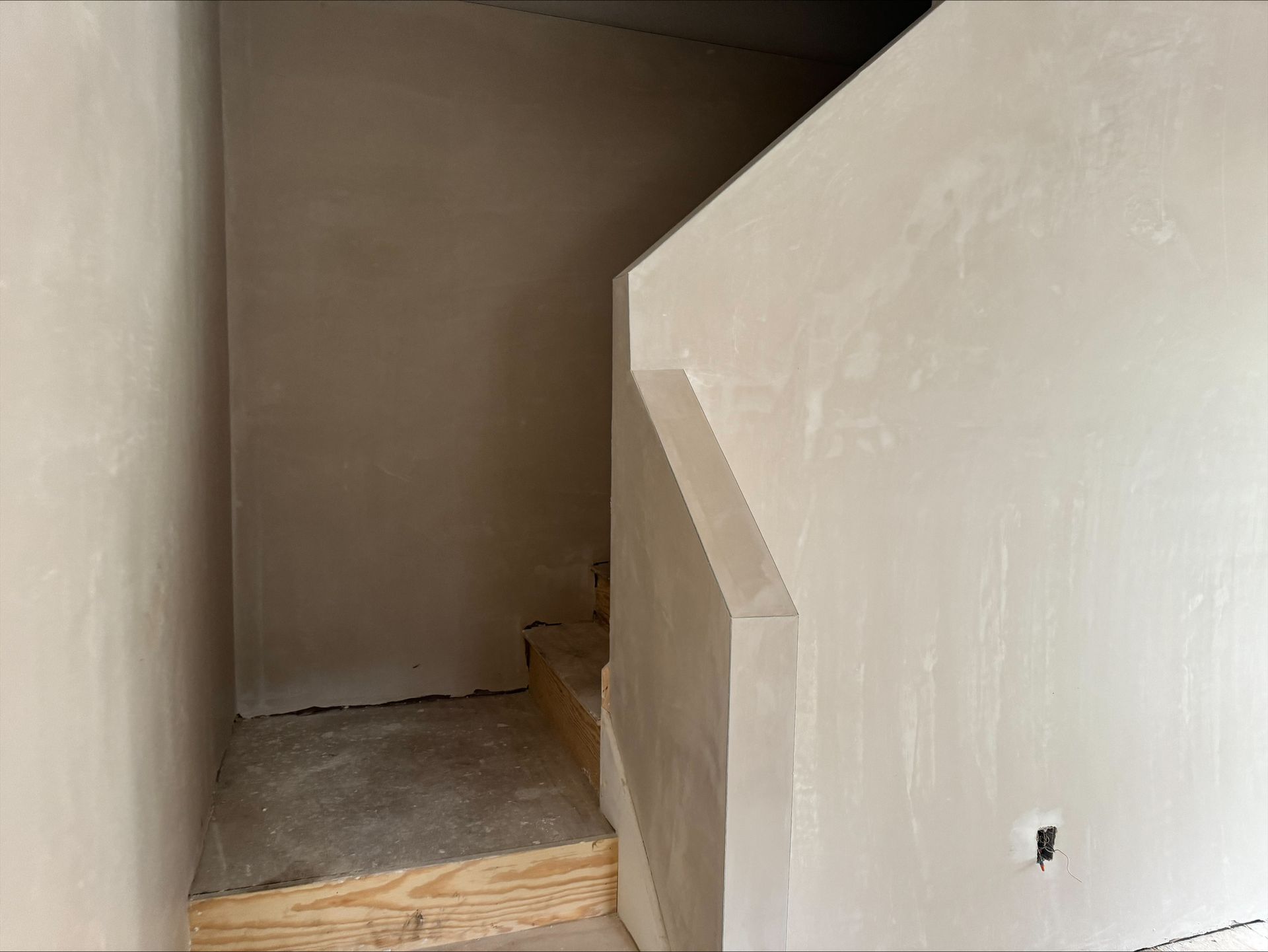 Unfinished interior stairwell with beige walls and wooden steps leading up to a landing