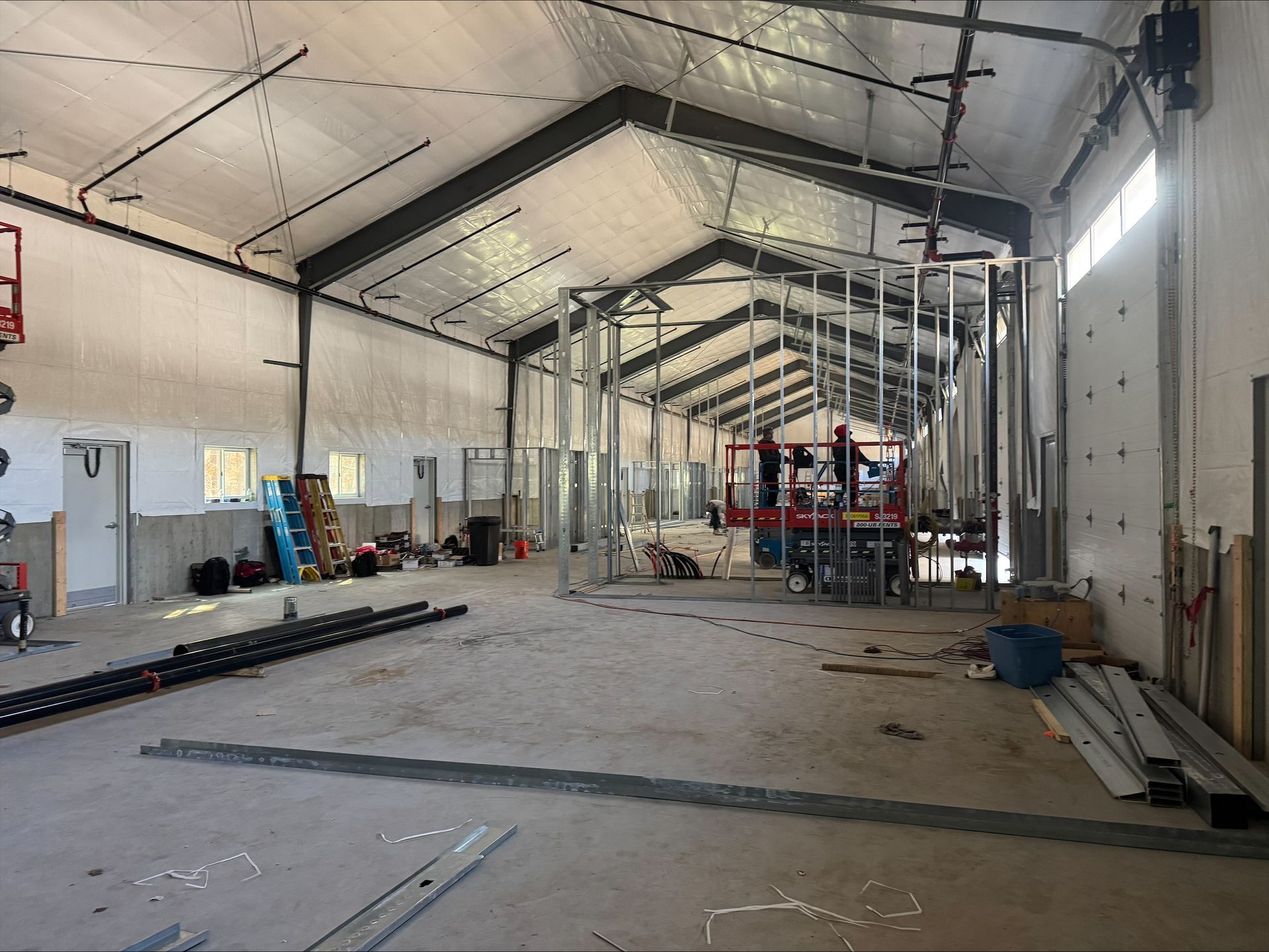 Large empty industrial warehouse with a high arched roof, scattered tools, and a work platform in the distance