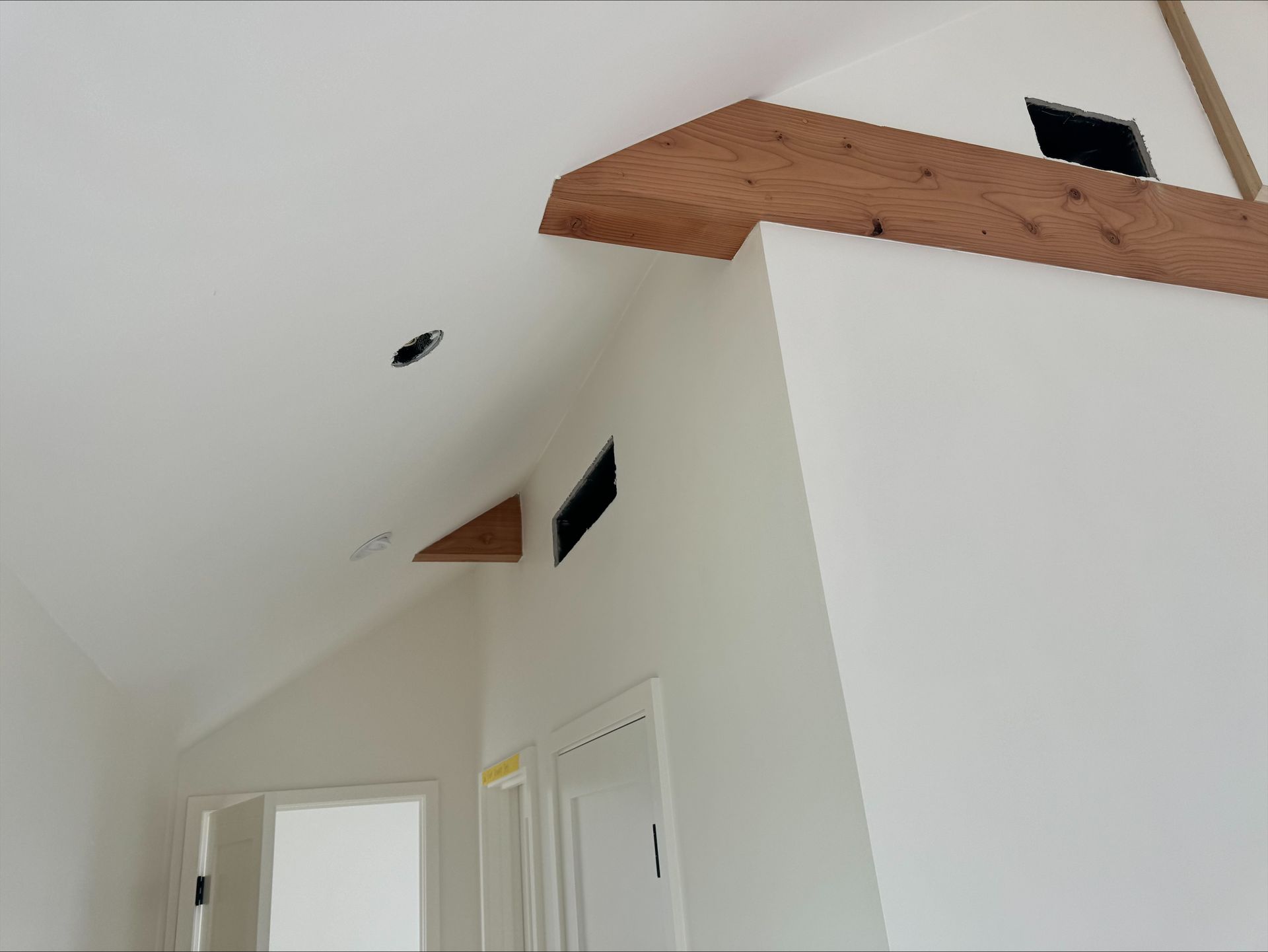 White vaulted ceiling with wooden beams and small black vents above a hallway and doorways