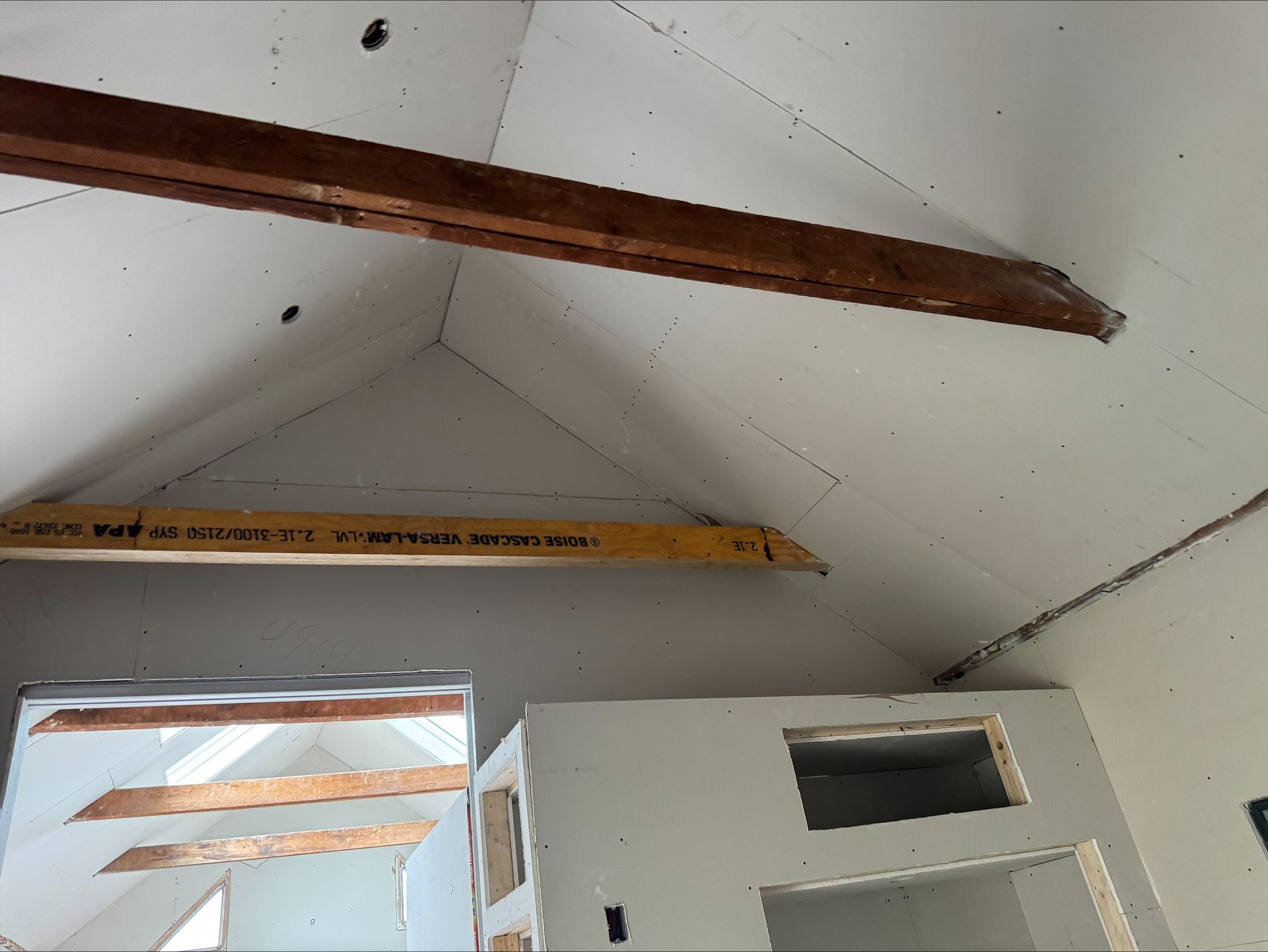 Partially finished room with exposed ceiling beams and a doorway below