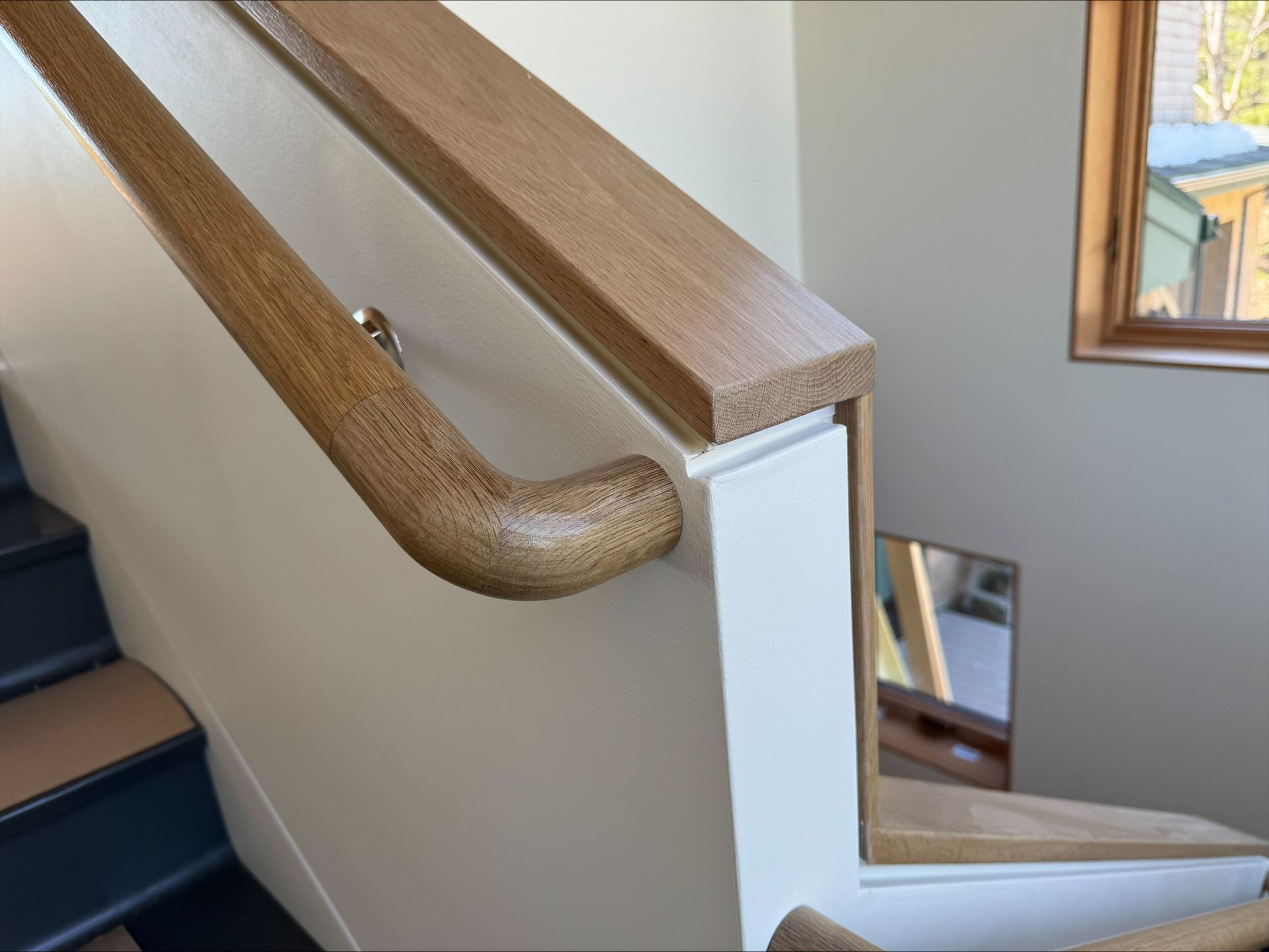 Wooden stair railing with curved corner beside a white interior staircase wall and mirror.