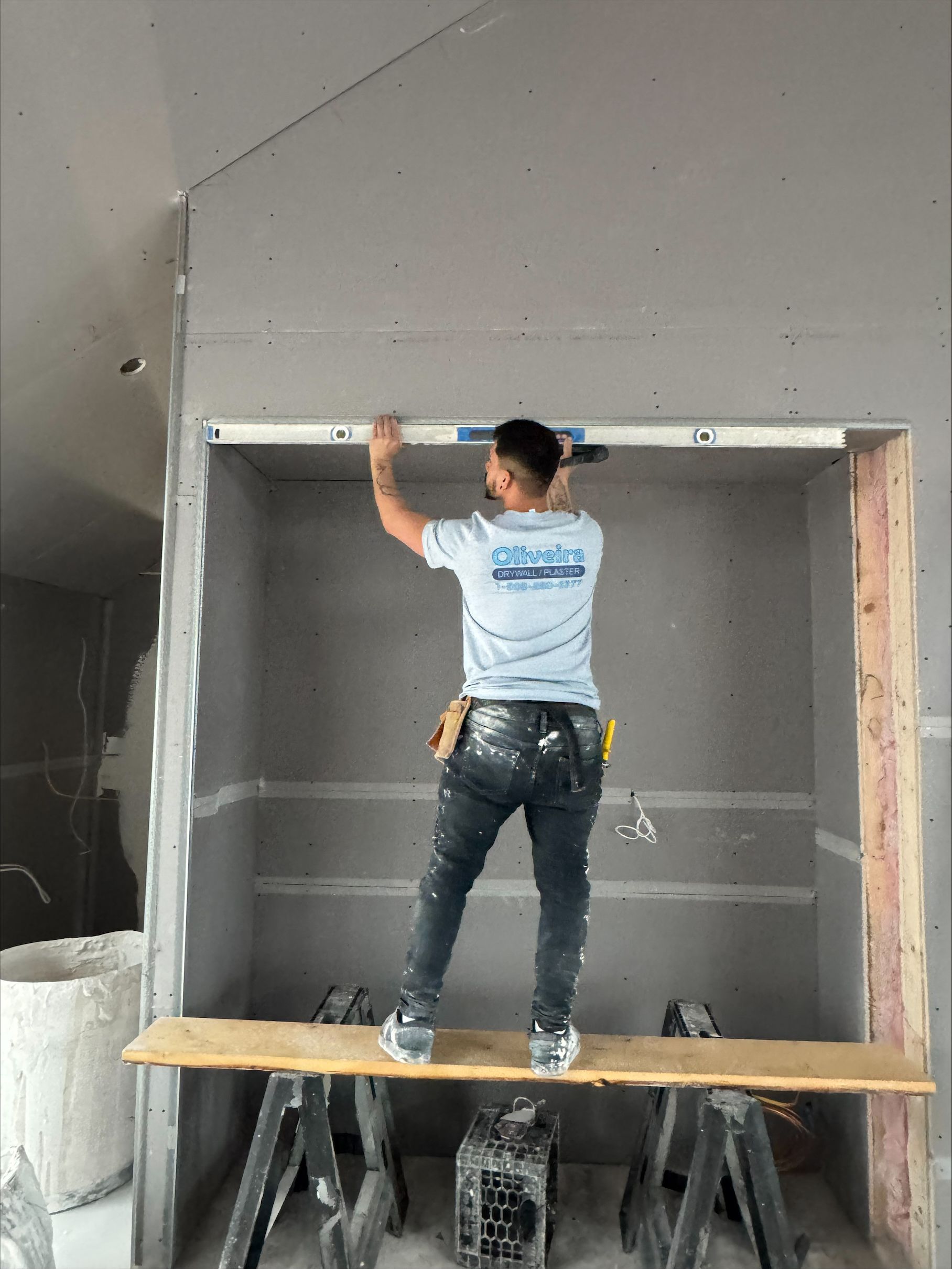 Worker on a scaffold installing a metal frame in a gray interior wall.