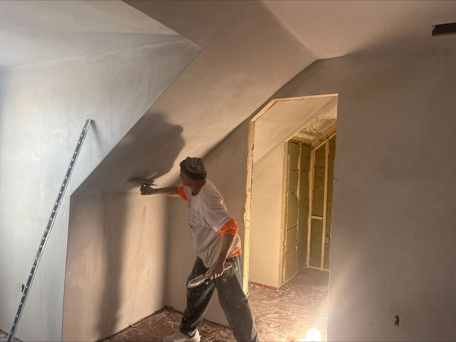 Worker painting a slanted ceiling and wall in a room under renovation